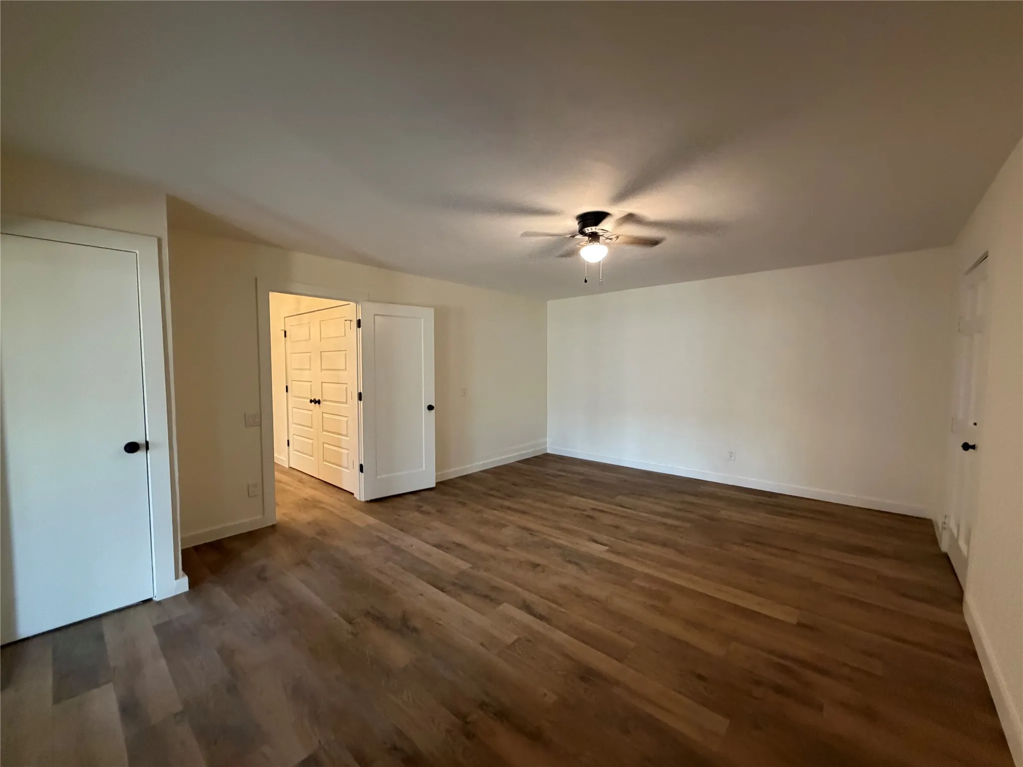 Expansive room featuring wood-finish flooring, light-toned walls, and a ceiling fan with integrated lighting