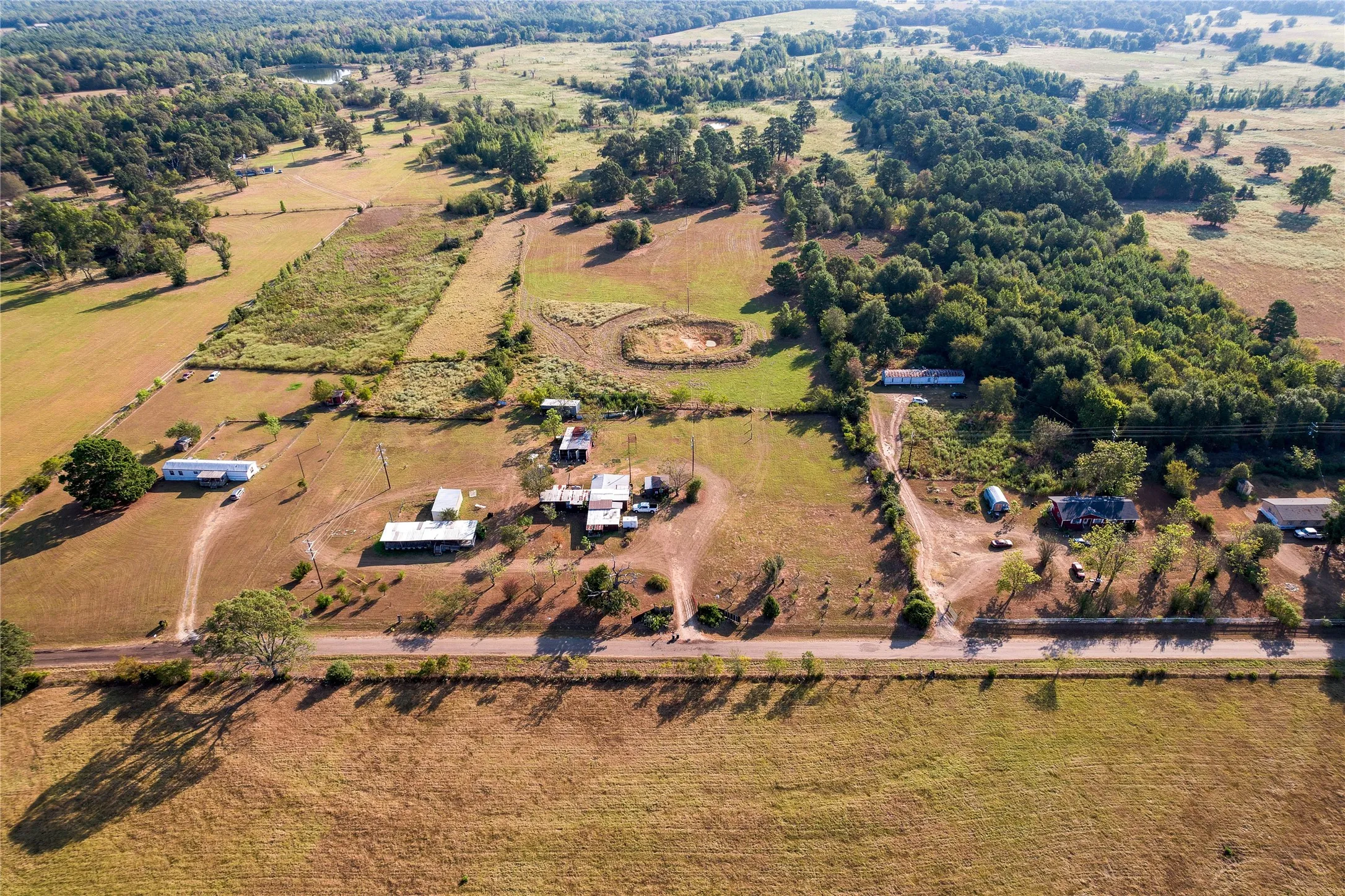 Expansive land parcel featuring open fields, wooded areas, and multiple structures