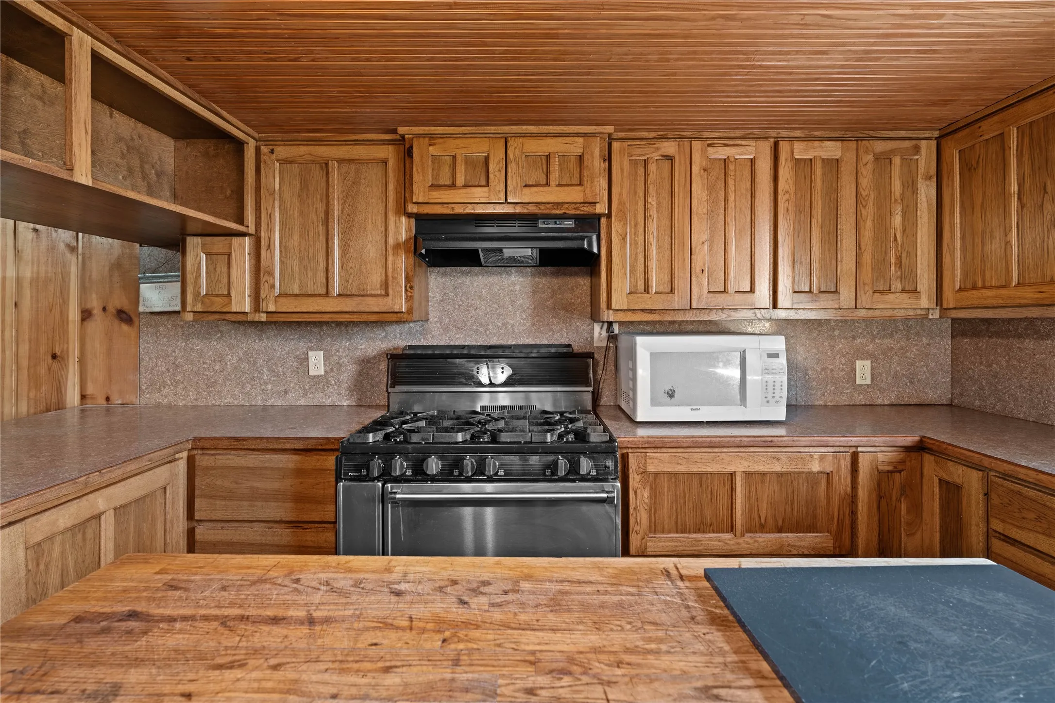 Wood plank ceiling, wood cabinetry, stainless steel range, built-in range hood, and ample countertop space
