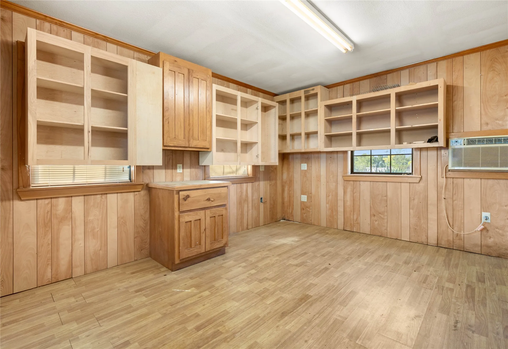 Wood-finish flooring, wood paneling, wood cabinetry, built-in shelving, and a fluorescent light fixture