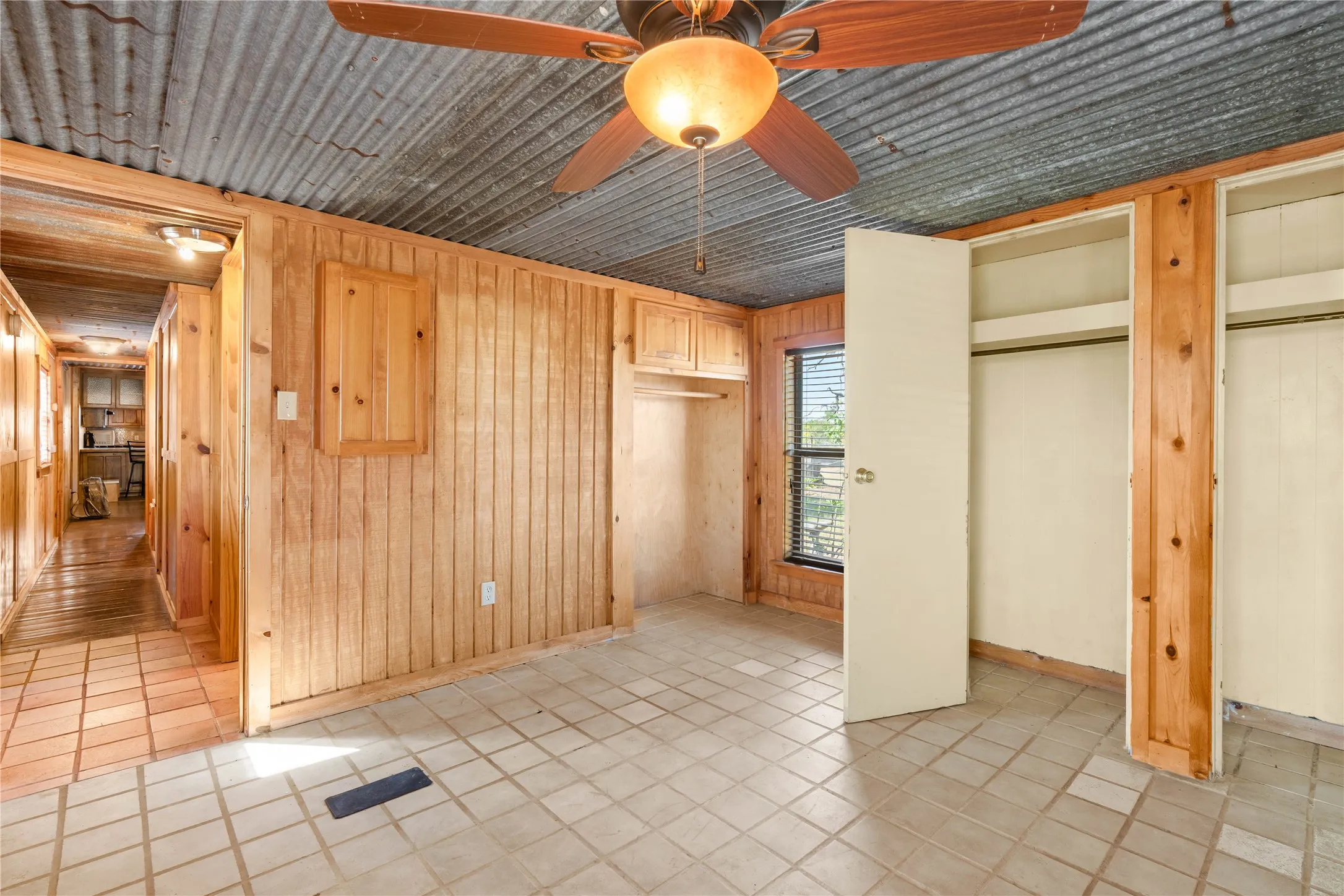 Corrugated metal ceiling, wood plank walls, tile flooring, built-in open shelving, and a ceiling fan with light fixture