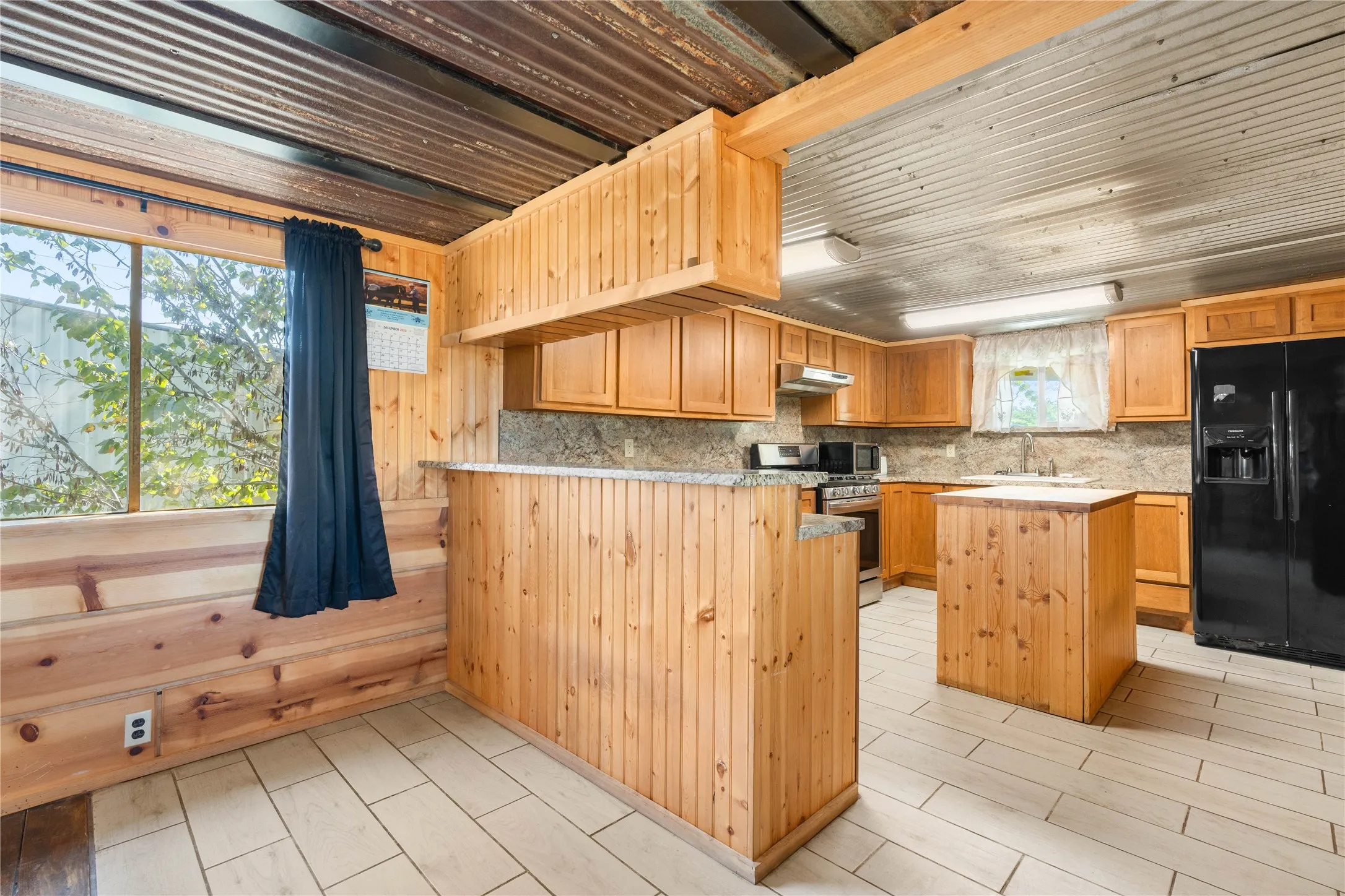 Kitchen featuring wood cabinetry, stainless steel appliances, a center island, and tile flooring