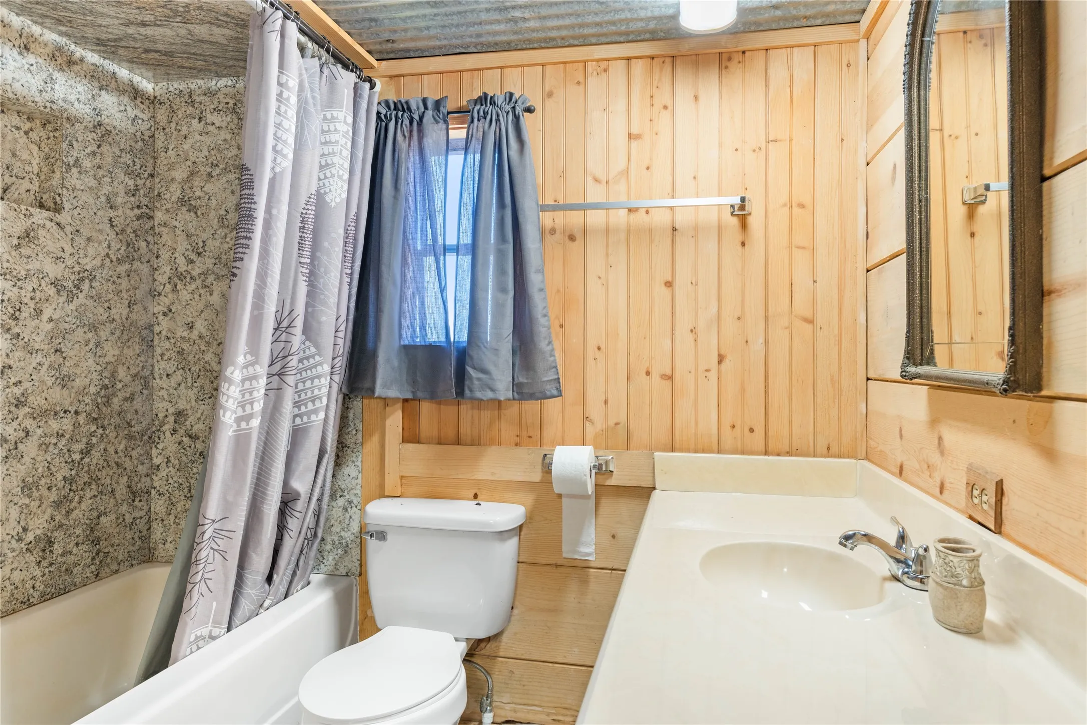 Bathroom featuring wood-paneled walls, a vanity with an integrated sink, a built-in bathtub with a textured surround, and a wall-mounted mirror