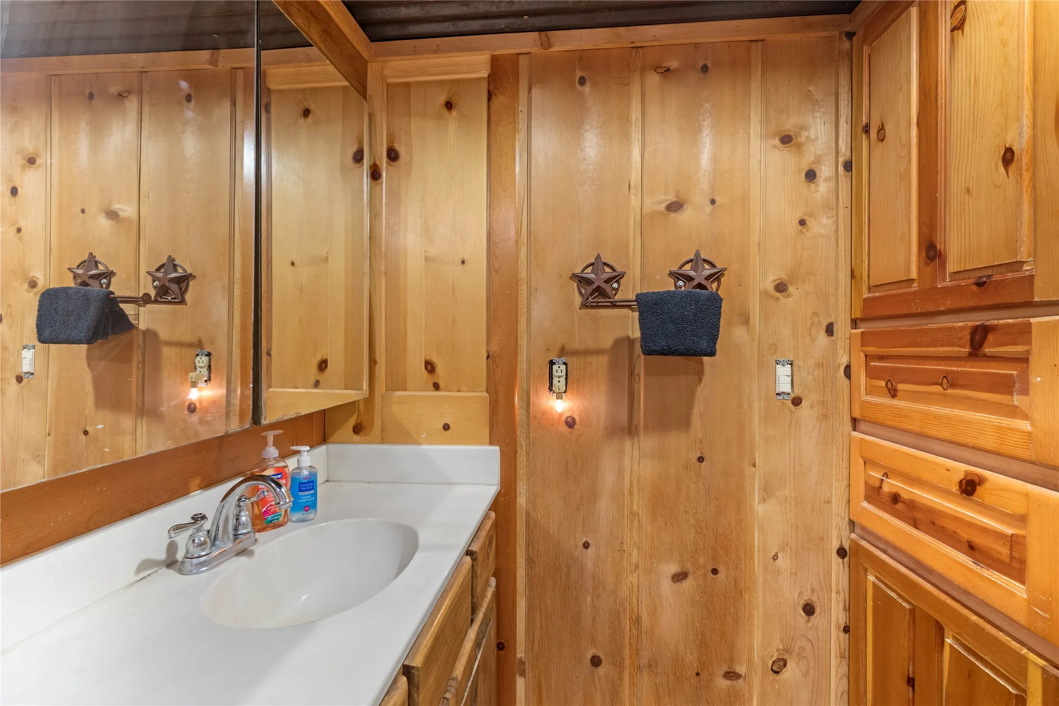 Wood paneling throughout, built-in storage cabinetry, vanity with integrated sink, wall-mounted mirror, and corrugated metal ceiling