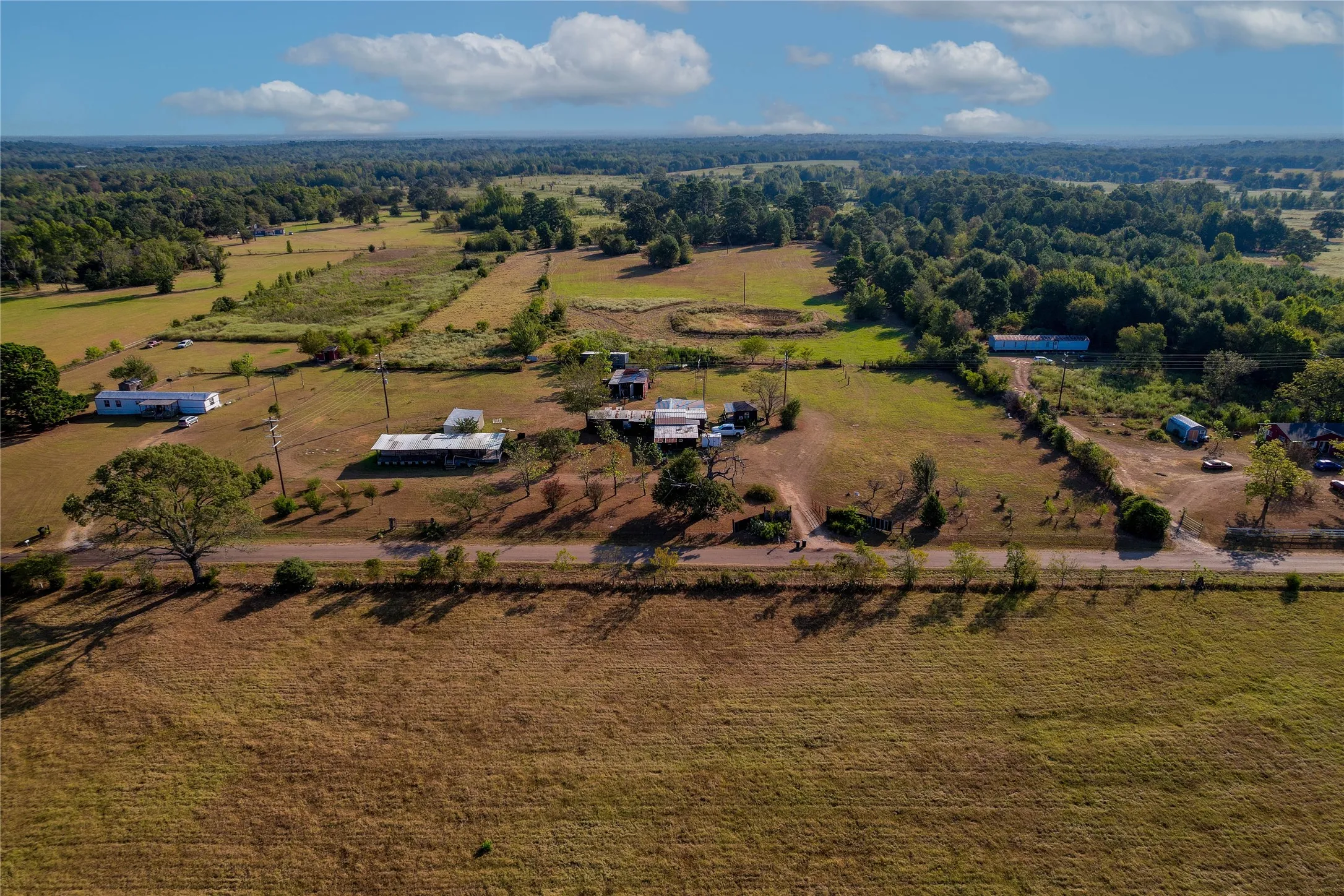 Expansive rural property featuring multiple structures, open fields, and mature tree lines