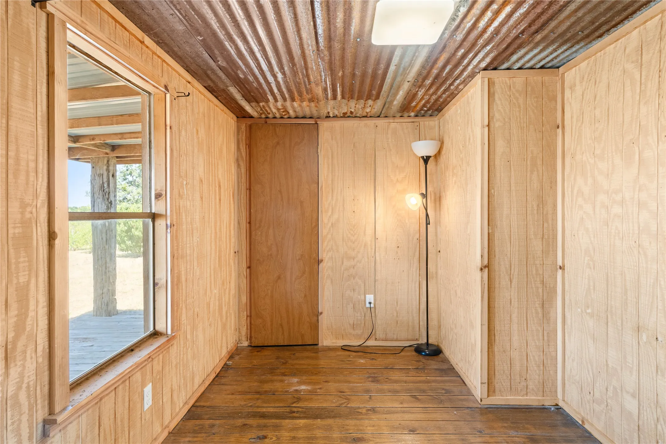 Corrugated metal ceiling, wood-finish wall paneling, wood-finish flooring, built-in overhead lighting, and window