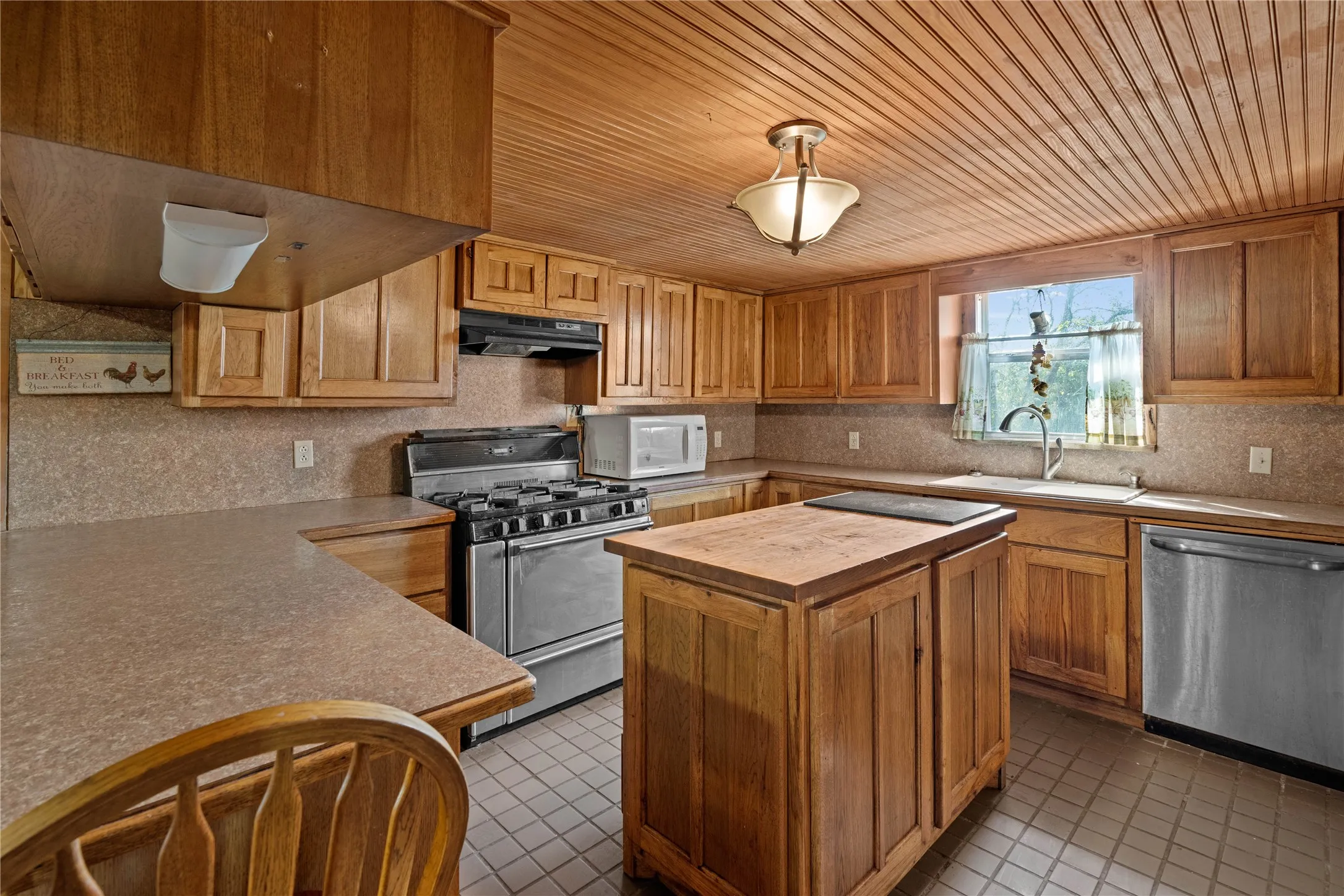 Kitchen featuring wood-paneled ceiling, wood cabinetry, stainless steel appliances, a center island, and a window