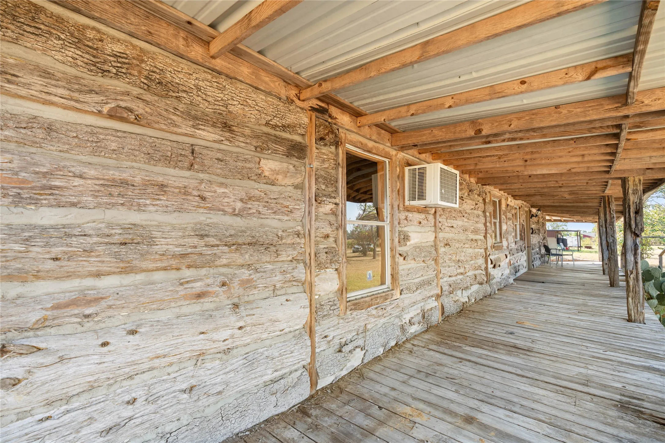 Expansive wood-finish porch with a corrugated metal roof, supported by natural wood pillars, complementing the horizontal log and stone exterior