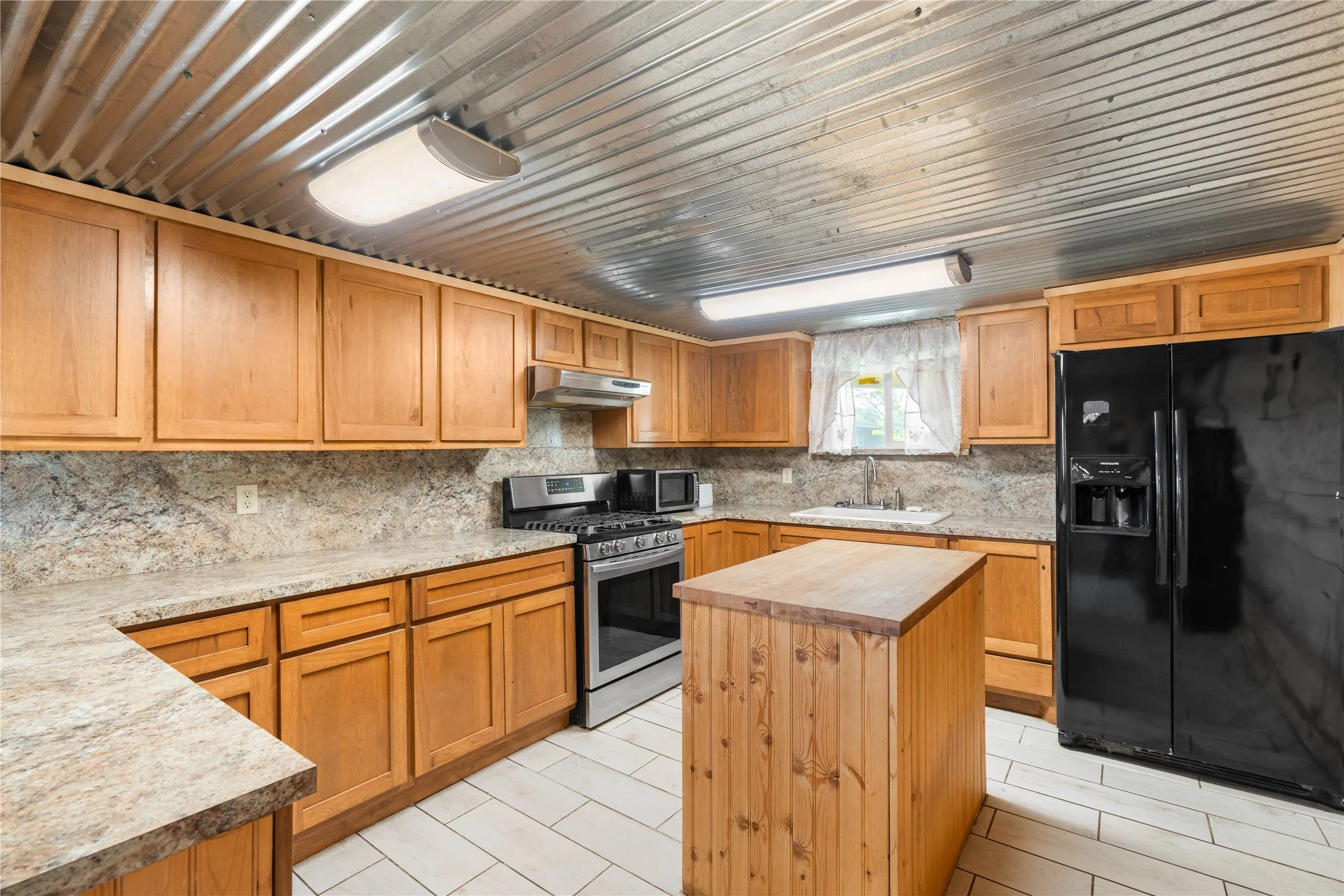 Kitchen featuring wood cabinetry, stone-look countertops, a stainless steel range, and a wood-panel island