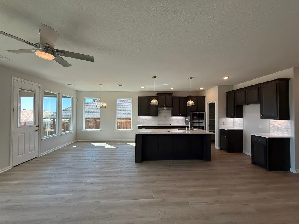 Open-concept living area featuring wood-finish flooring, a contemporary ceiling fan, and multiple windows