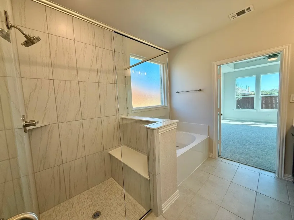 Walk-in shower with a built-in bench and glass enclosure, separate soaking tub, and tile flooring