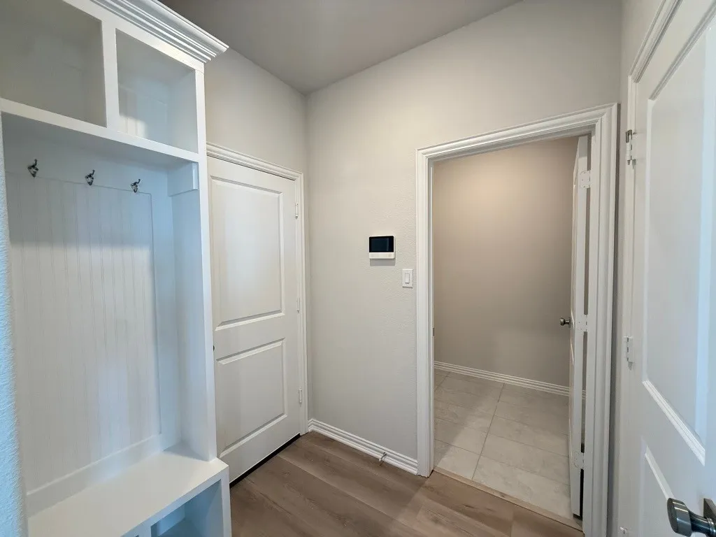 Built-in storage bench with upper shelving and coat hooks, wood-finish flooring, and white paneled doors