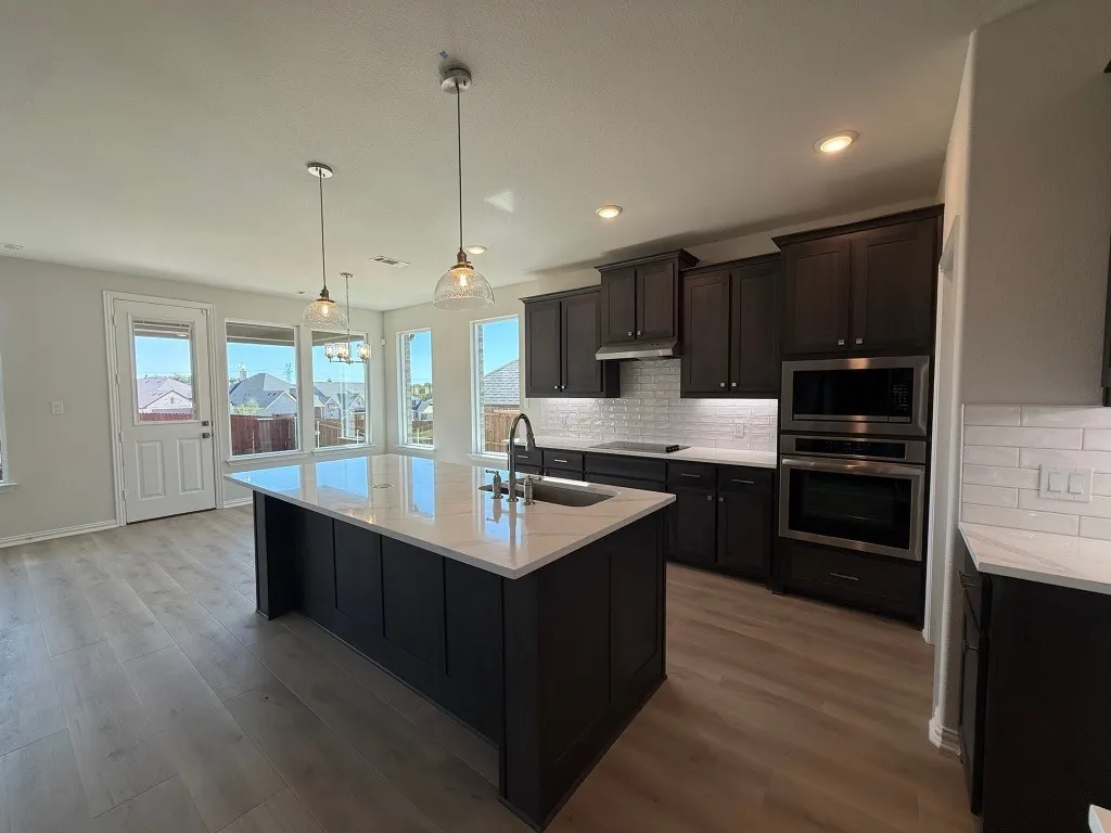 Kitchen featuring an oversized island with pendant lighting, dark wood cabinetry, stainless steel appliances, and wood-finish flooring