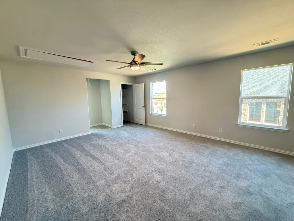 Spacious room featuring gray carpeting, a ceiling fan with integrated lighting, two windows, and an open closet with shelving