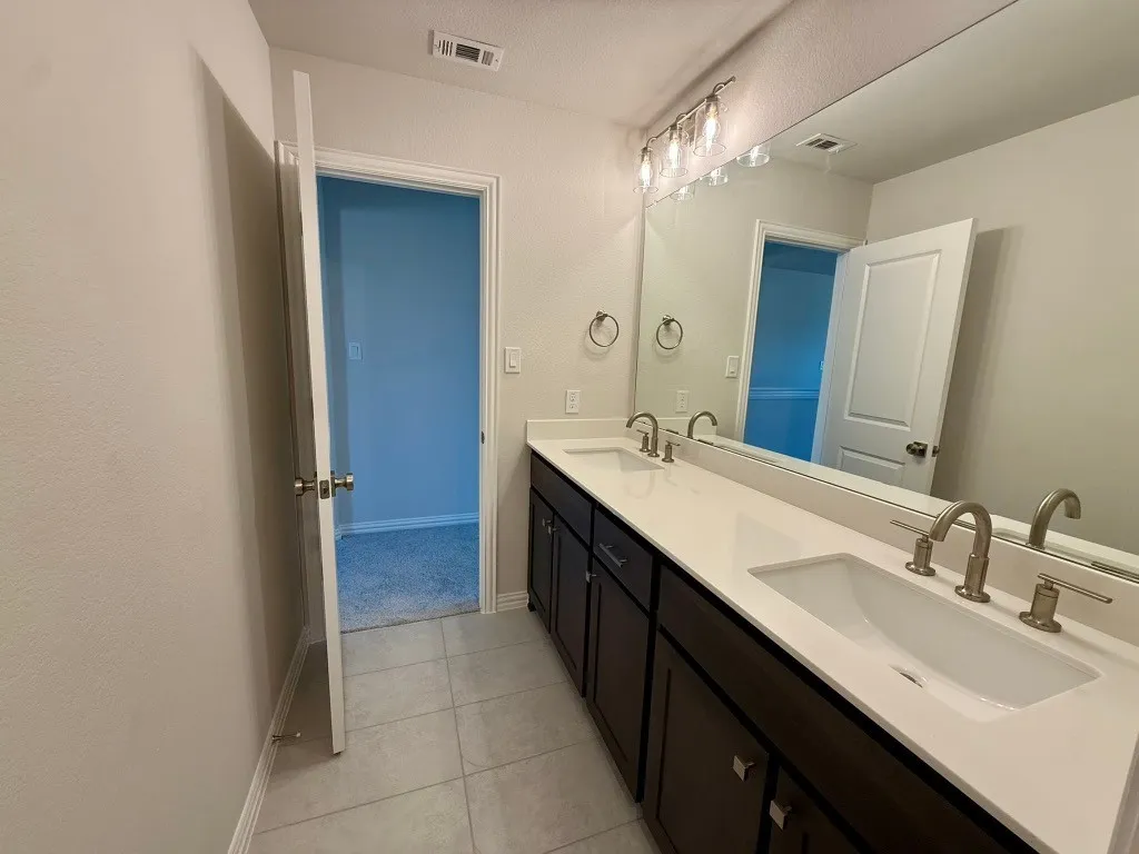 Dual vanity with integrated sinks, brushed nickel fixtures, dark wood-finish cabinetry, a full-width mirror, and overhead lighting