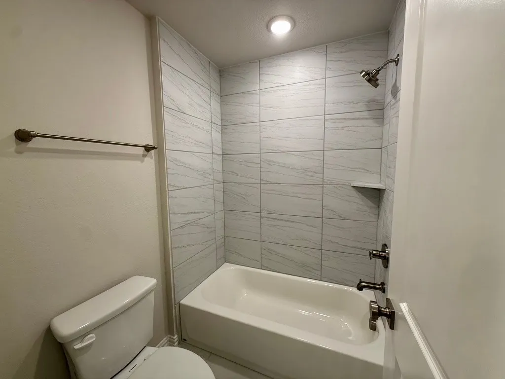 White tiled shower with built-in shelf, white bathtub, and brushed nickel fixtures