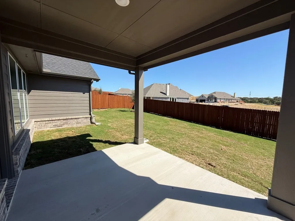 Covered concrete patio with recessed lighting, offering direct access to a fenced backyard with a wood privacy fence