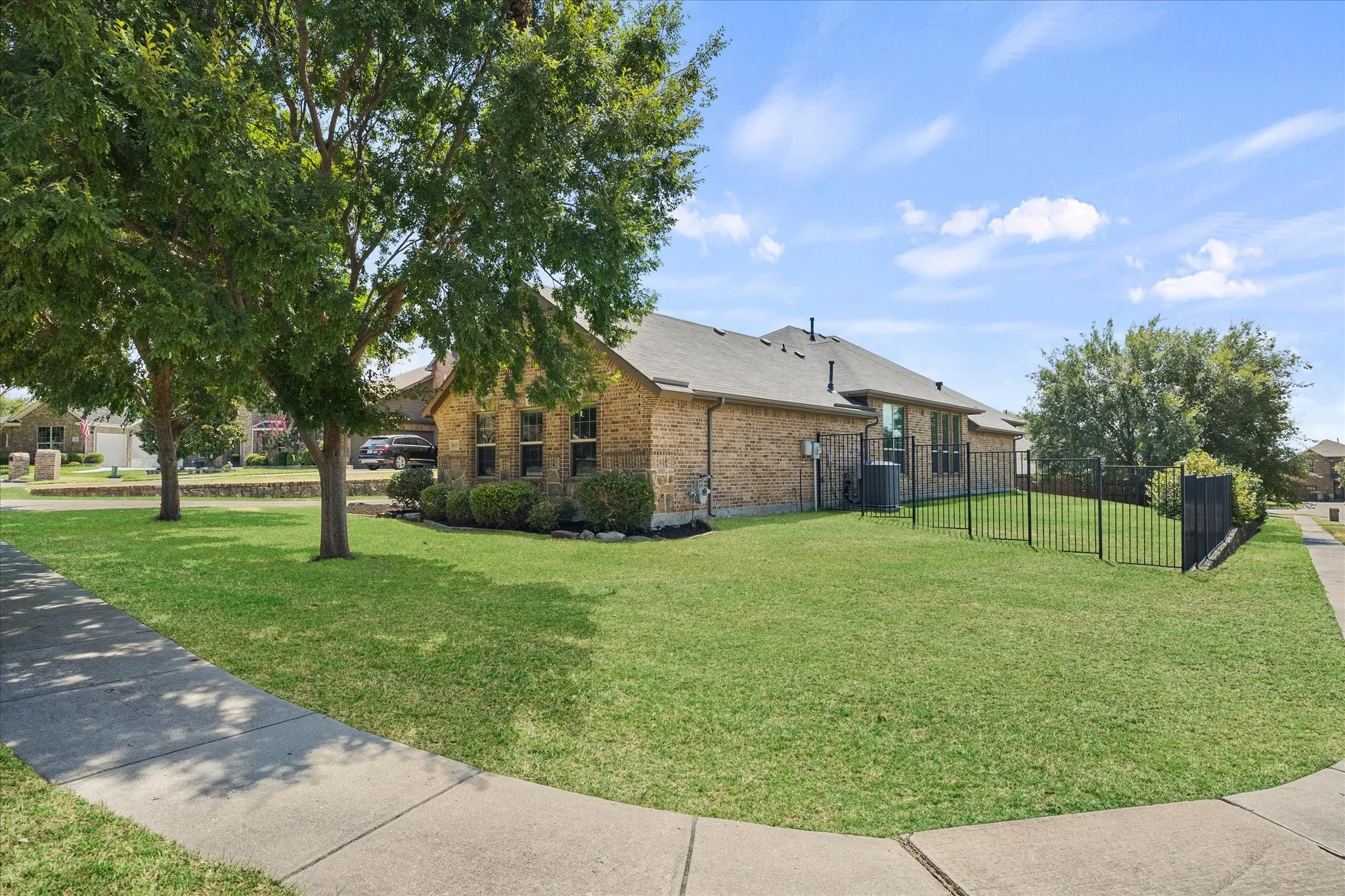 Brick exterior with a dark-pitched roof, featuring multiple windows, mature trees, and a black metal fence