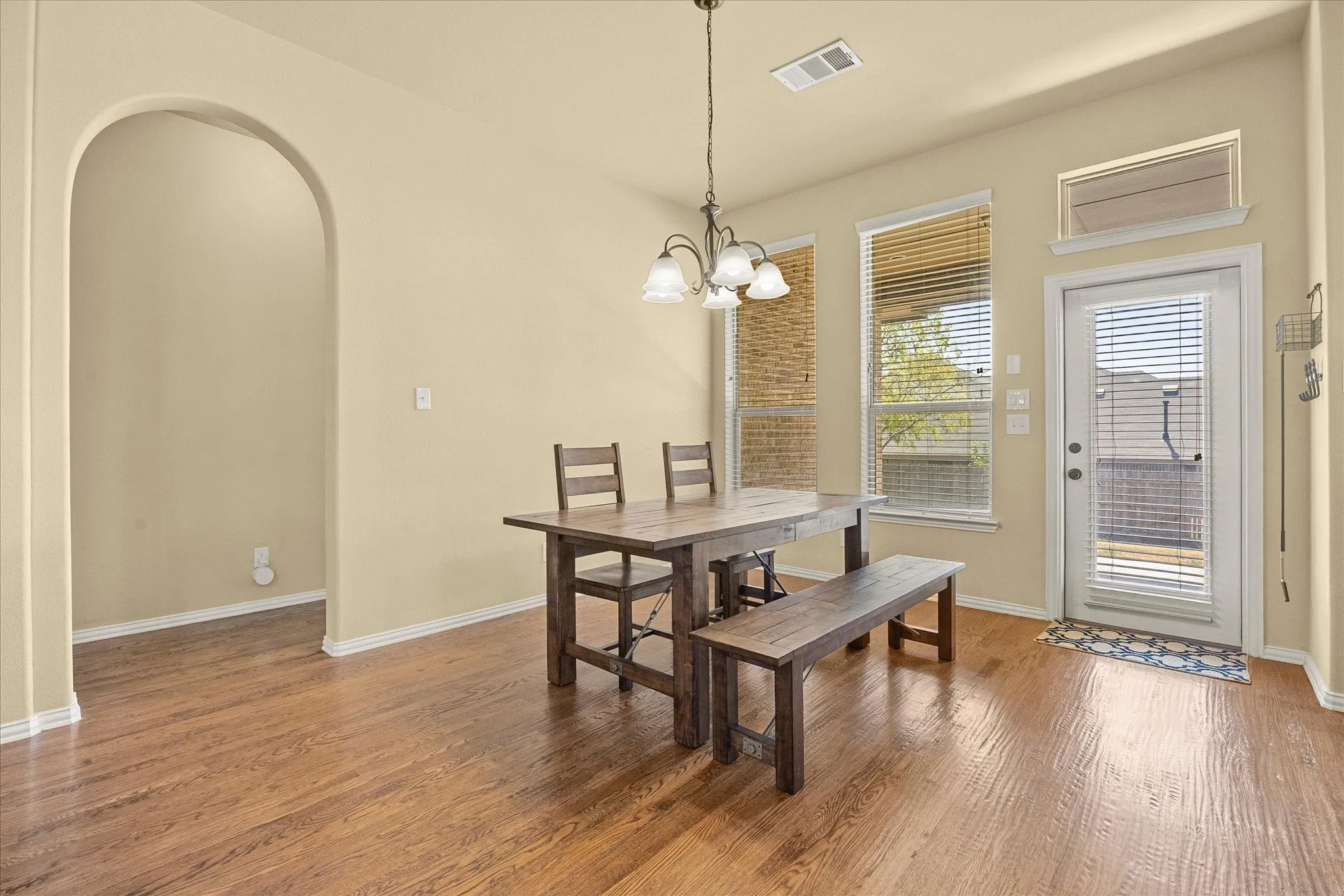 Spacious dining area featuring warm wood-finish flooring, a pendant light fixture, and abundant natural light from multiple glass doors and windows
