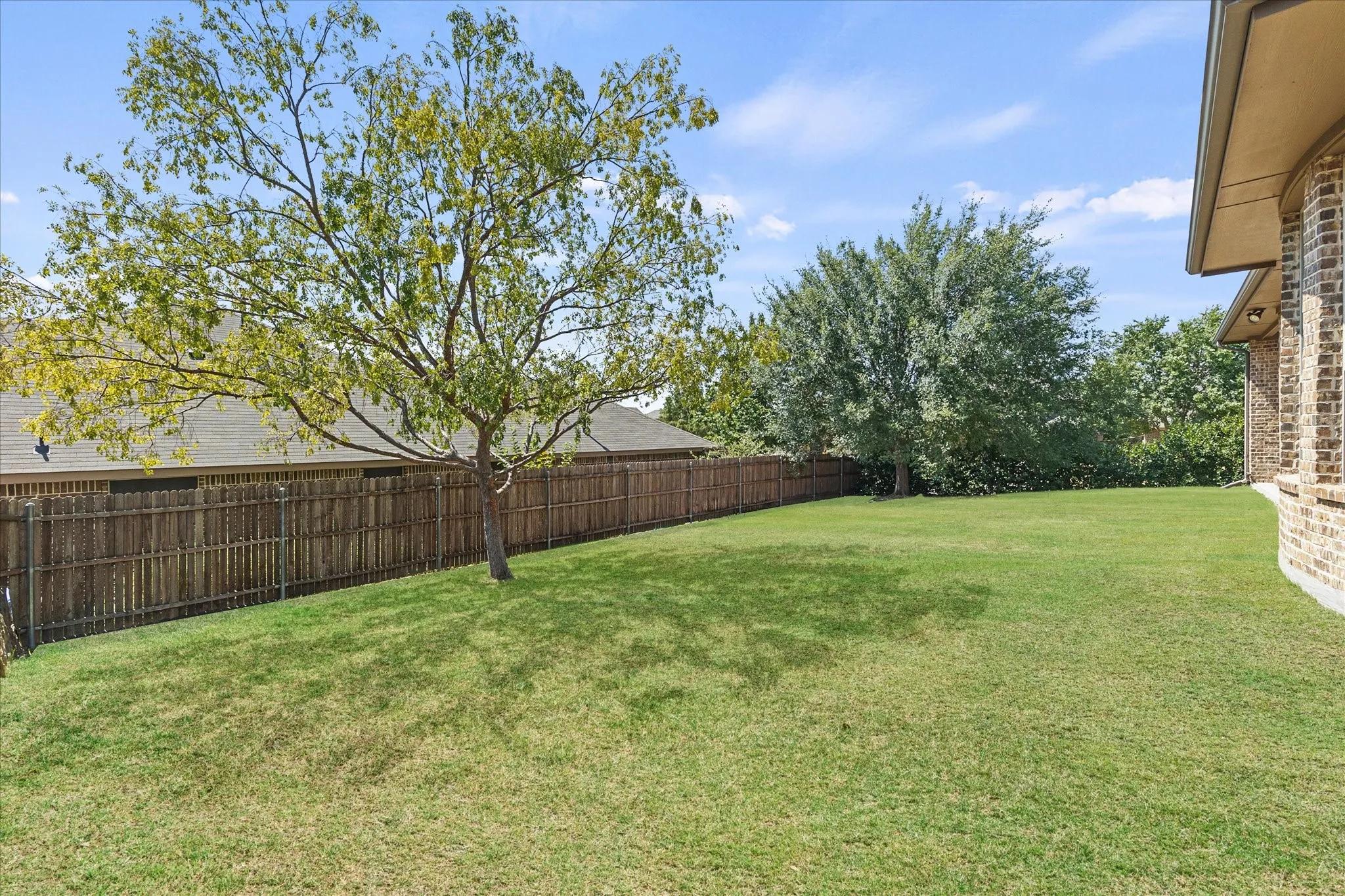 Expansive grassy yard featuring a mature tree, privacy fencing, and brick exterior detail