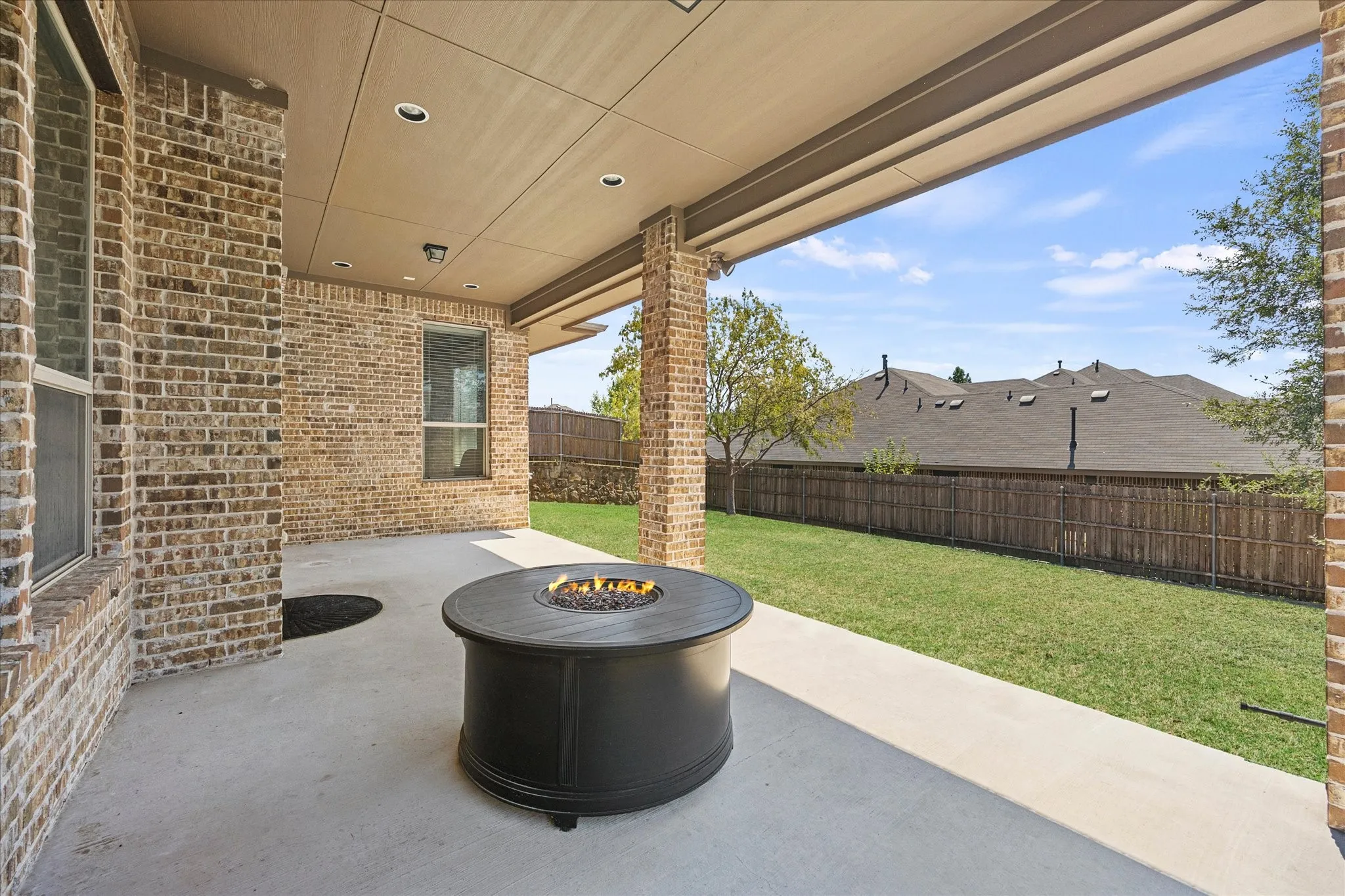 Covered patio with a built-in fire pit, brick exterior, recessed lighting, and a fenced backyard