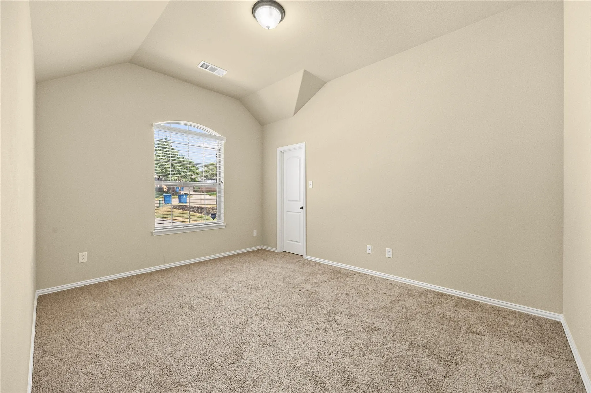 Vaulted ceiling, arched window, neutral wall paint, carpet flooring, flush mount lighting fixture