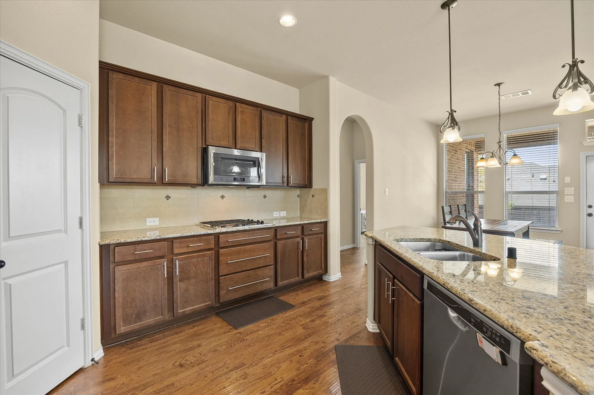 Kitchen featuring wood-finish flooring, granite countertops, wood cabinetry, a built-in microwave, and a stainless steel dishwasher
