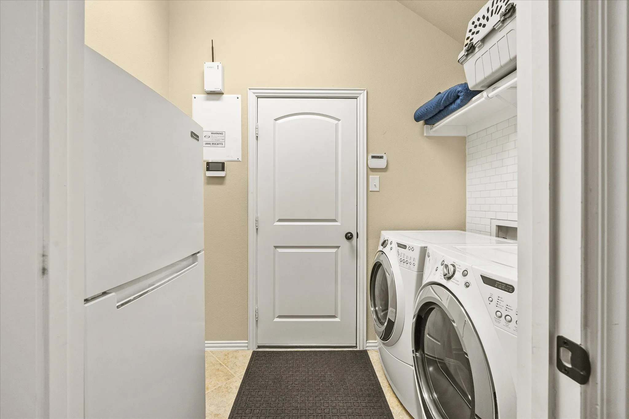 Laundry area featuring white appliances, wall-mounted shelving, white subway tile backsplash, and tile flooring