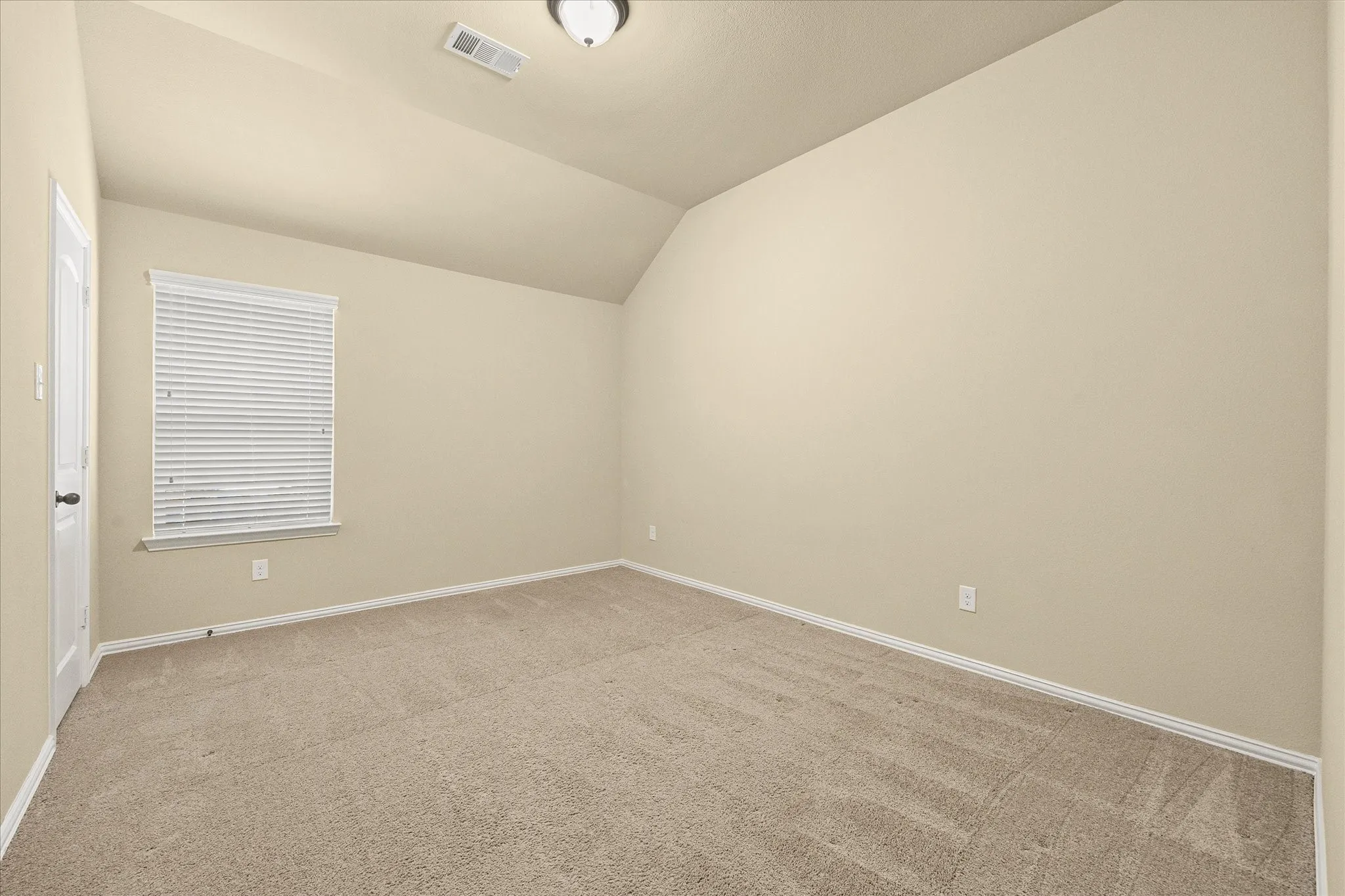 Carpeted room featuring a window with blinds, a white door, and a ceiling-mounted light​​‌​​​​‌​​‌‌​‌‌​​​‌‌​‌​‌​‌​​​‌​​ fixture