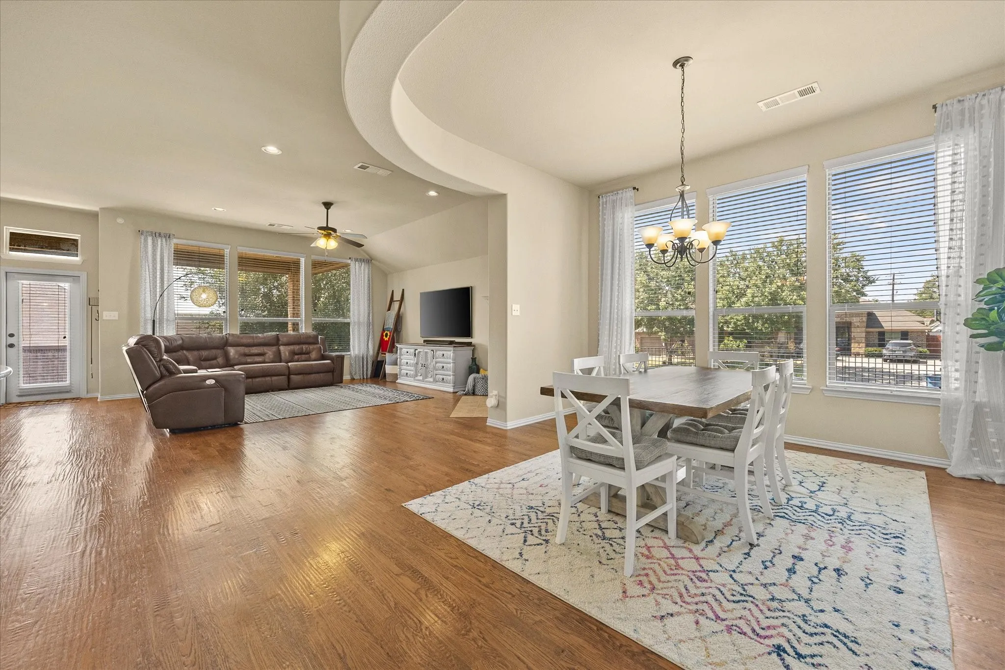 Open-concept living space featuring wood-finish flooring, a recessed ceiling detail, and a dining area with a chandelier