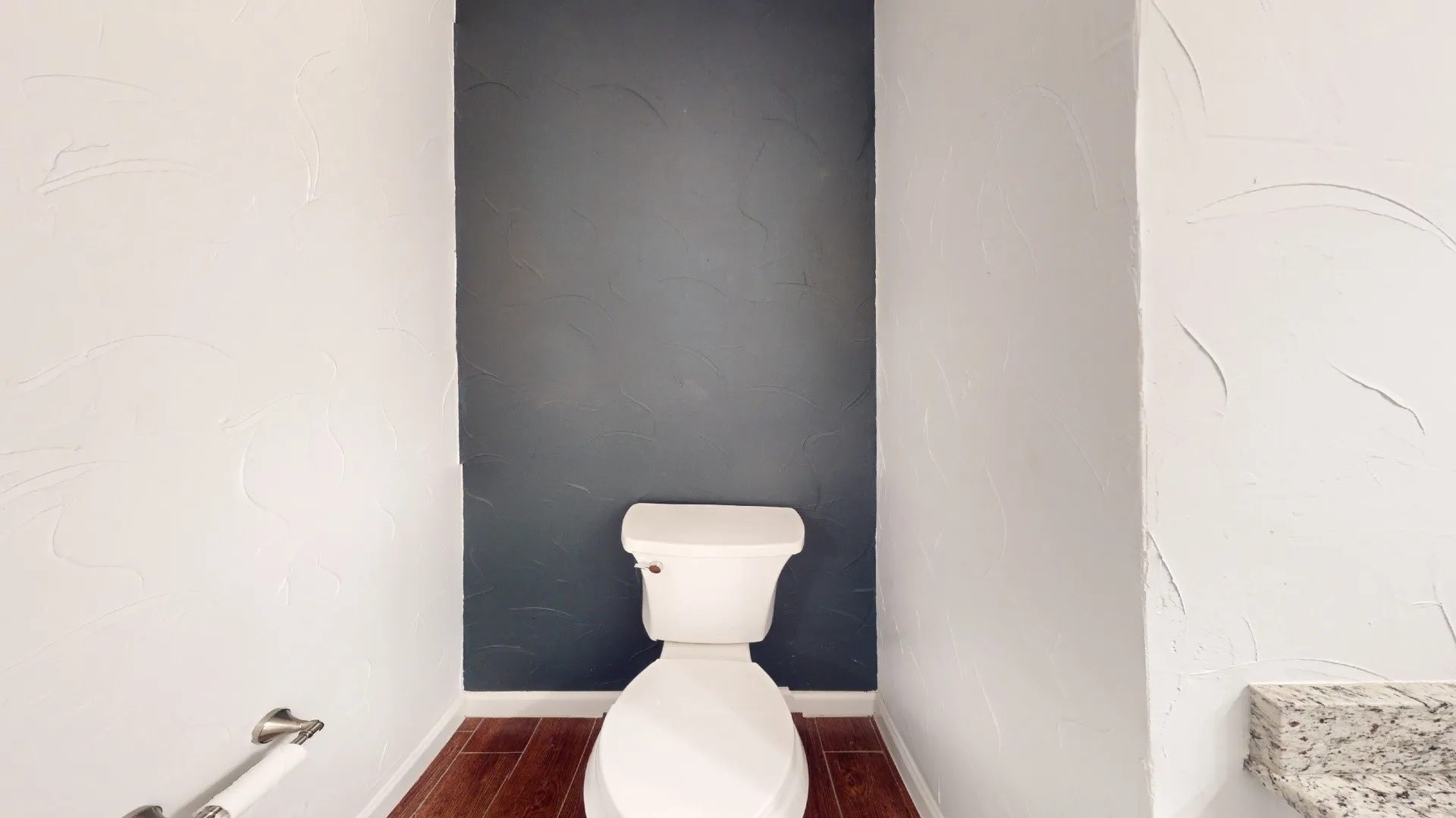 Wood-finish flooring with a white toilet and a granite countertop