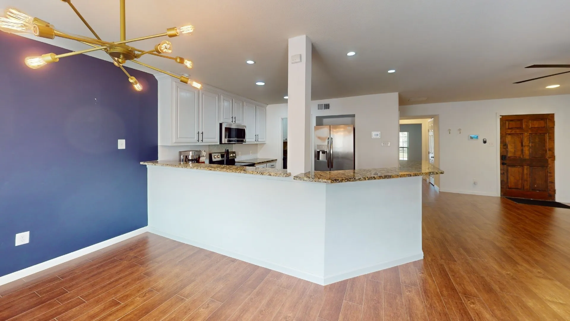 Wood-finish flooring, white cabinetry, integrated stainless steel appliances, and a spacious kitchen peninsula with a stone-finish countertop