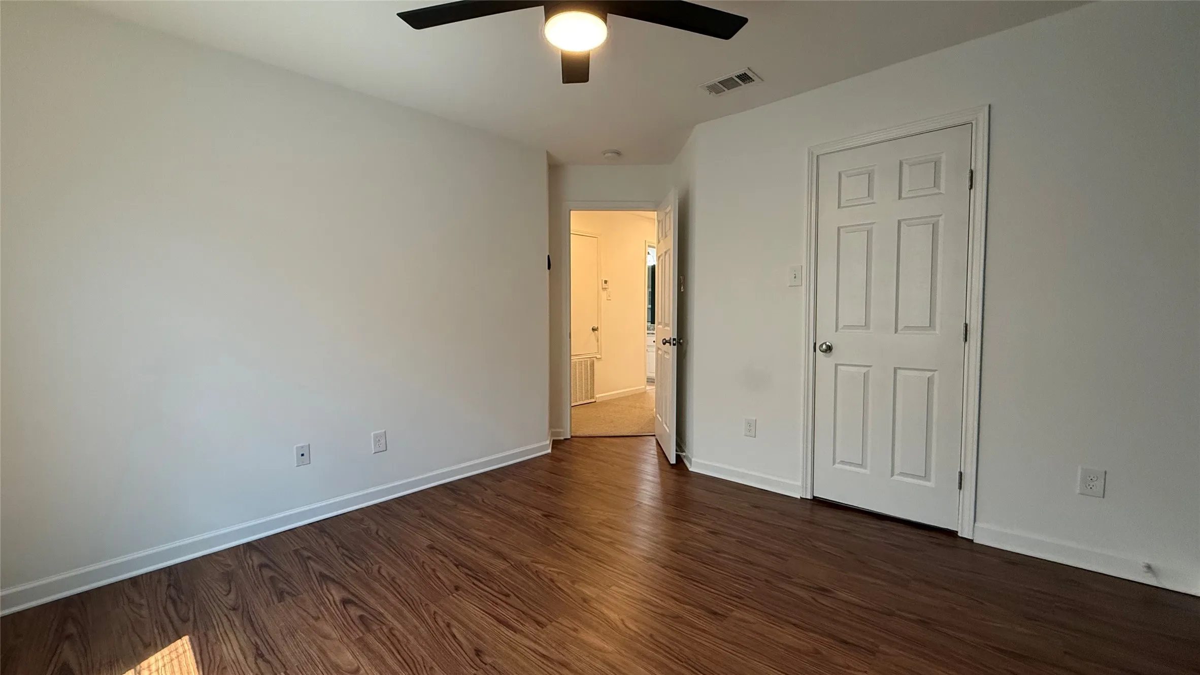 Wood-finish flooring, white paneled door, and a ceiling fan with integrated lighting