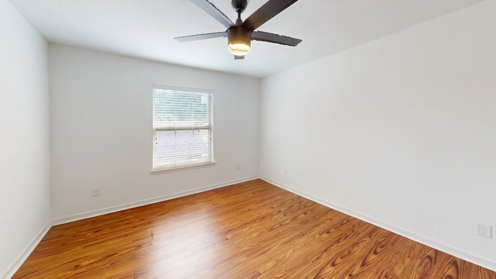 Hardwood-finish flooring, white walls, single window with blinds, and a ceiling fan with integrated lighting