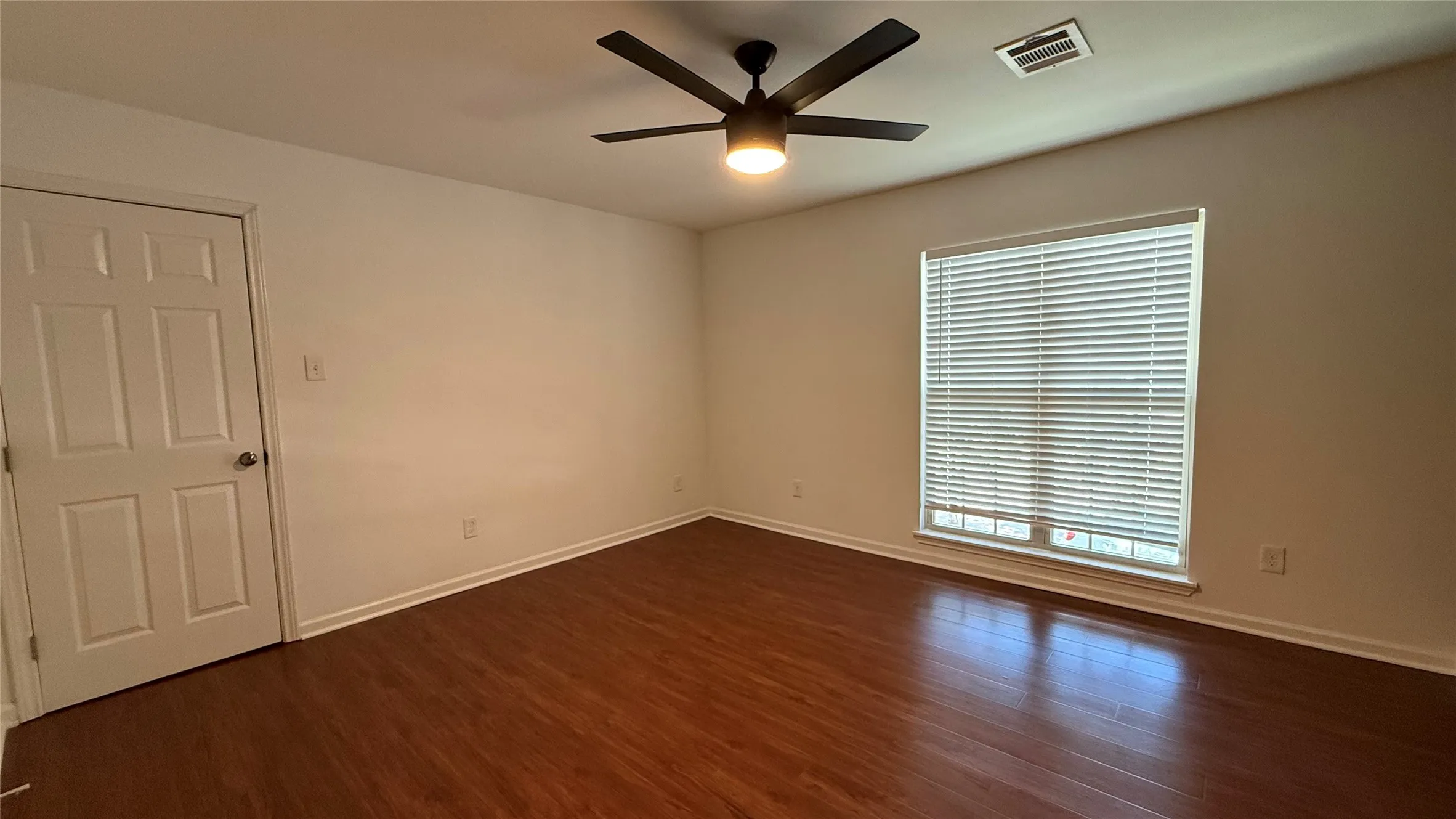 Wood-finish flooring with white baseboards, a six-panel door, and a window with blinds