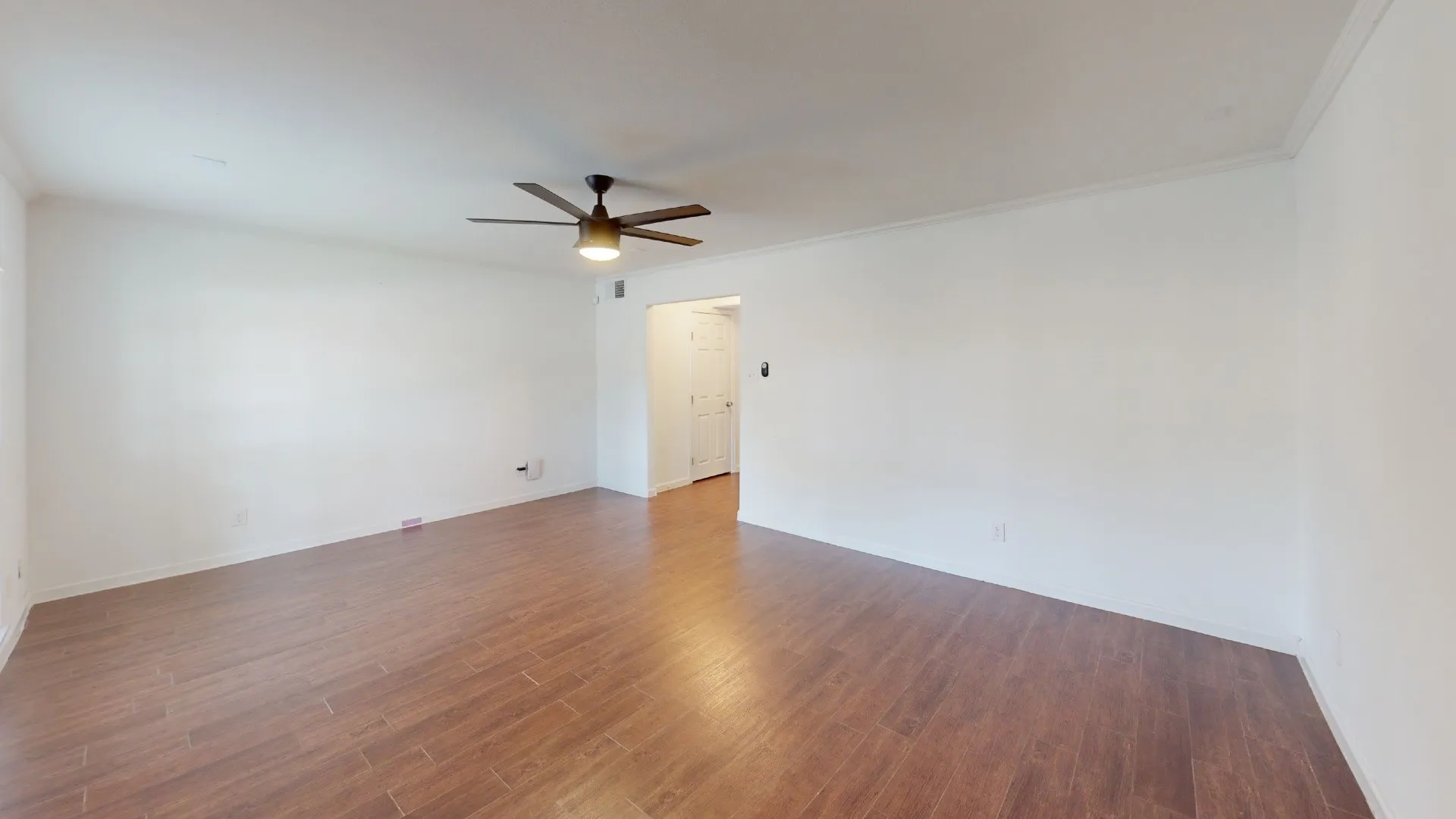 Spacious interior featuring wood-finish flooring, white walls, and a ceiling fan with integrated lighting