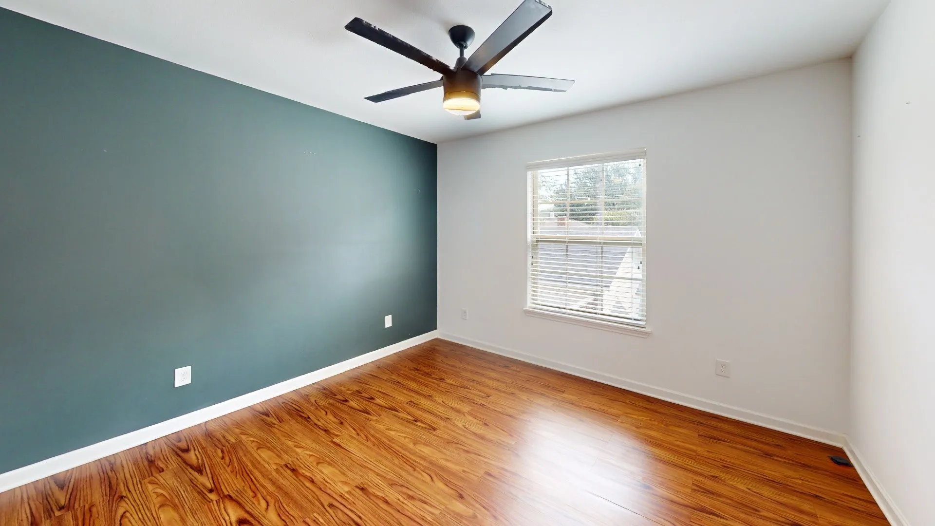 Wood-finish flooring, ceiling fan with integrated lighting, window with blinds, and a contrasting accent wall