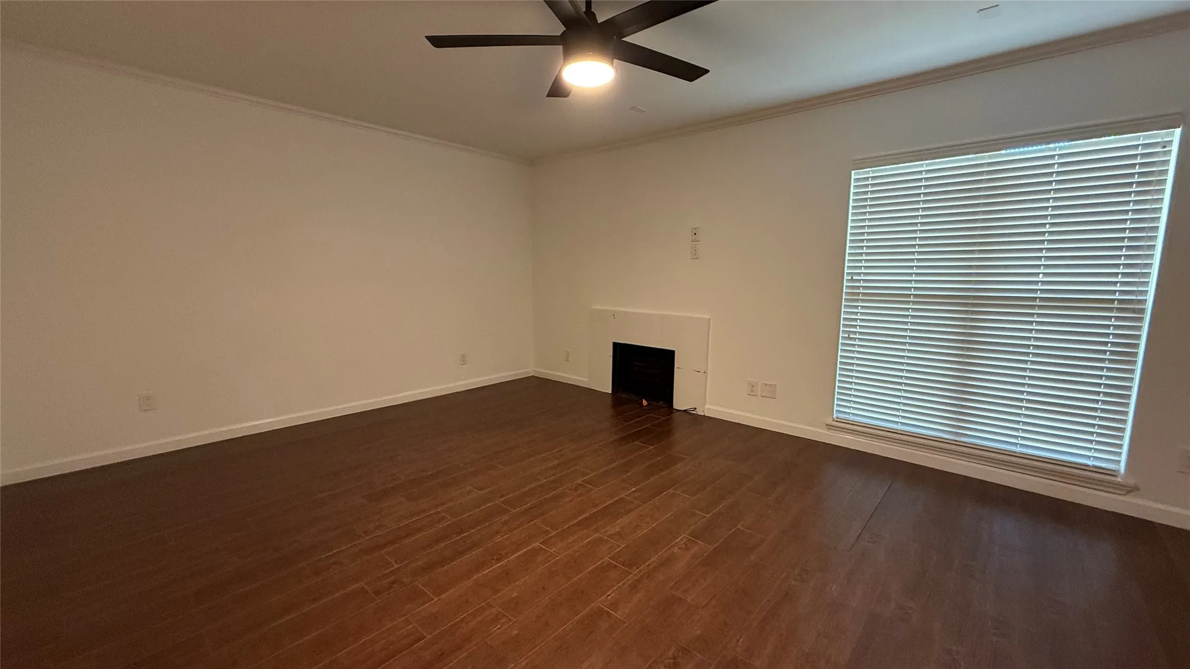 Expansive room featuring wood-finish flooring, a built-in fireplace, a large window with horizontal blinds, and a ceiling fan with integrated lighting