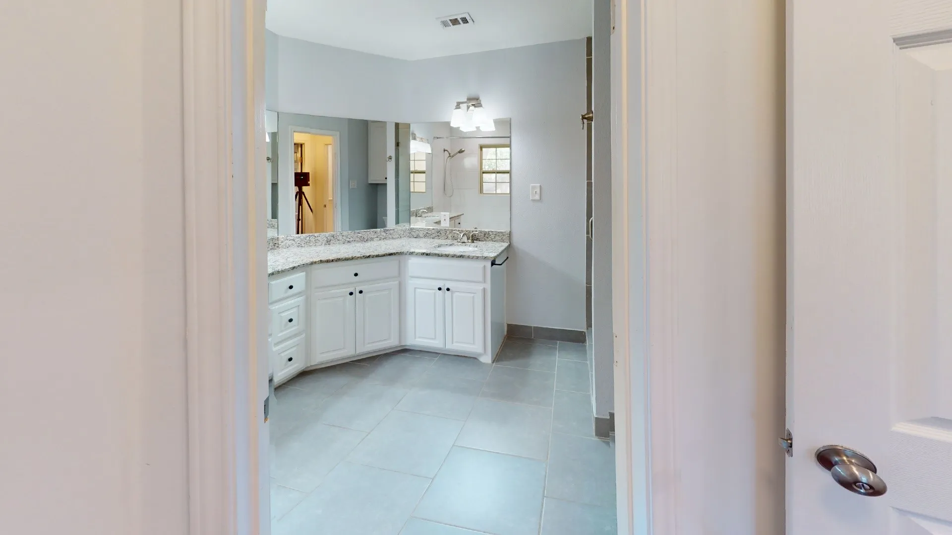Dual vanity with white cabinetry, granite-style countertop, and expansive wall-mounted mirror