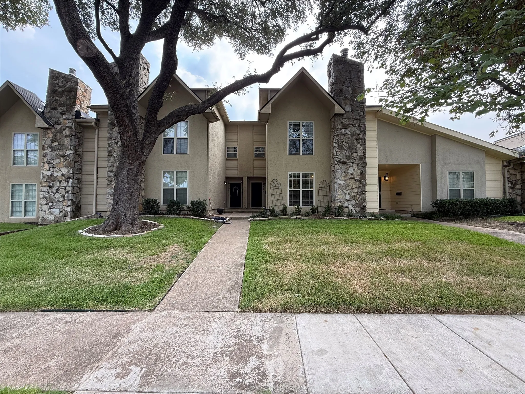 Two-story residence featuring stucco and stone veneer exterior, multiple gabled rooflines, and a concrete walkway