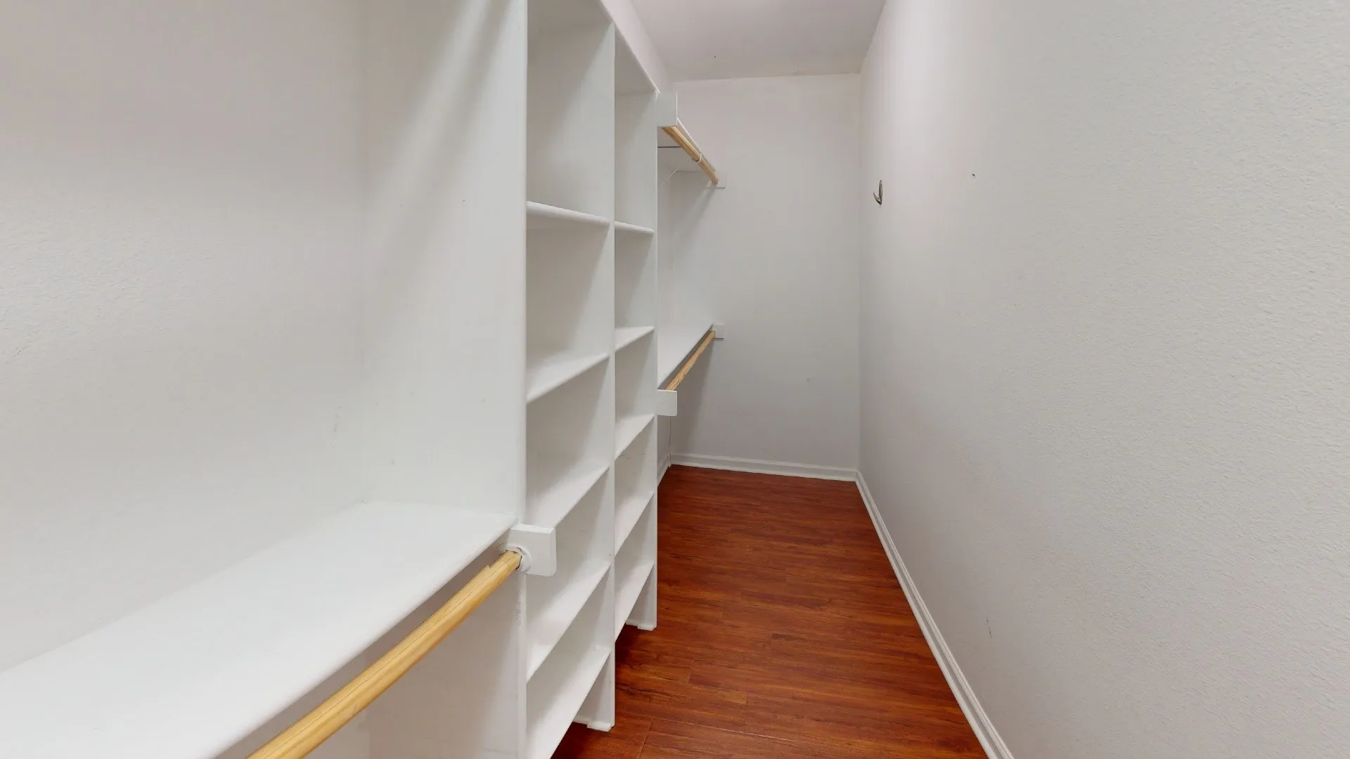 Walk-in closet with extensive built-in shelving, hanging rods, and wood-finish flooring