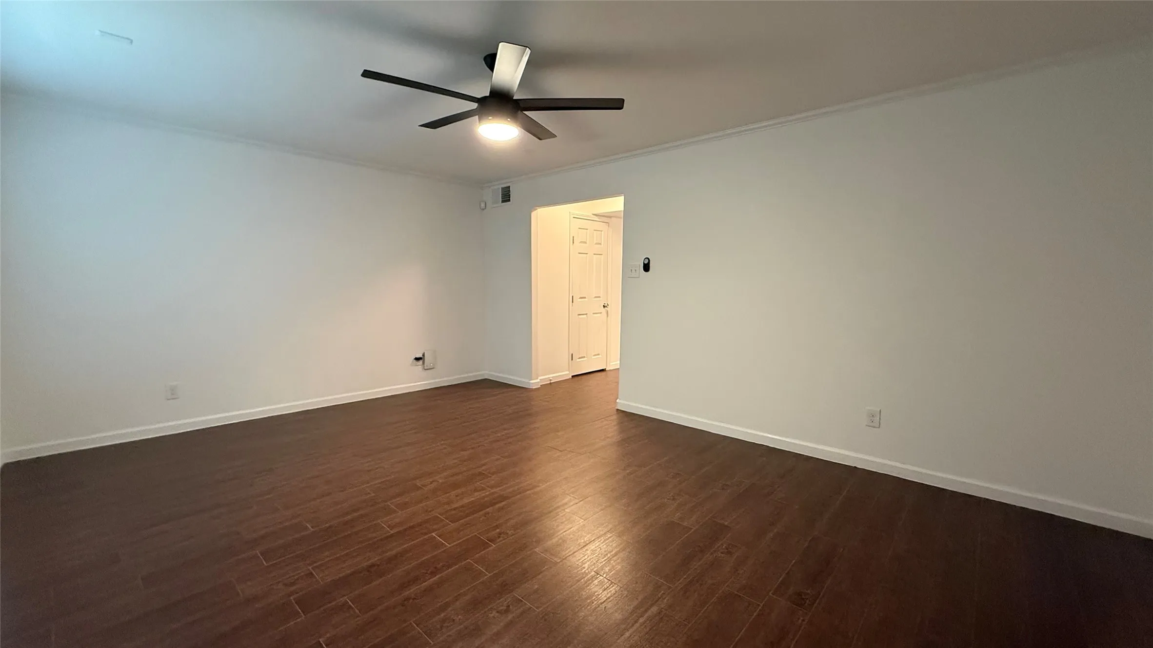 Spacious room featuring wood-finish flooring, a ceiling fan with integrated lighting, and crown molding