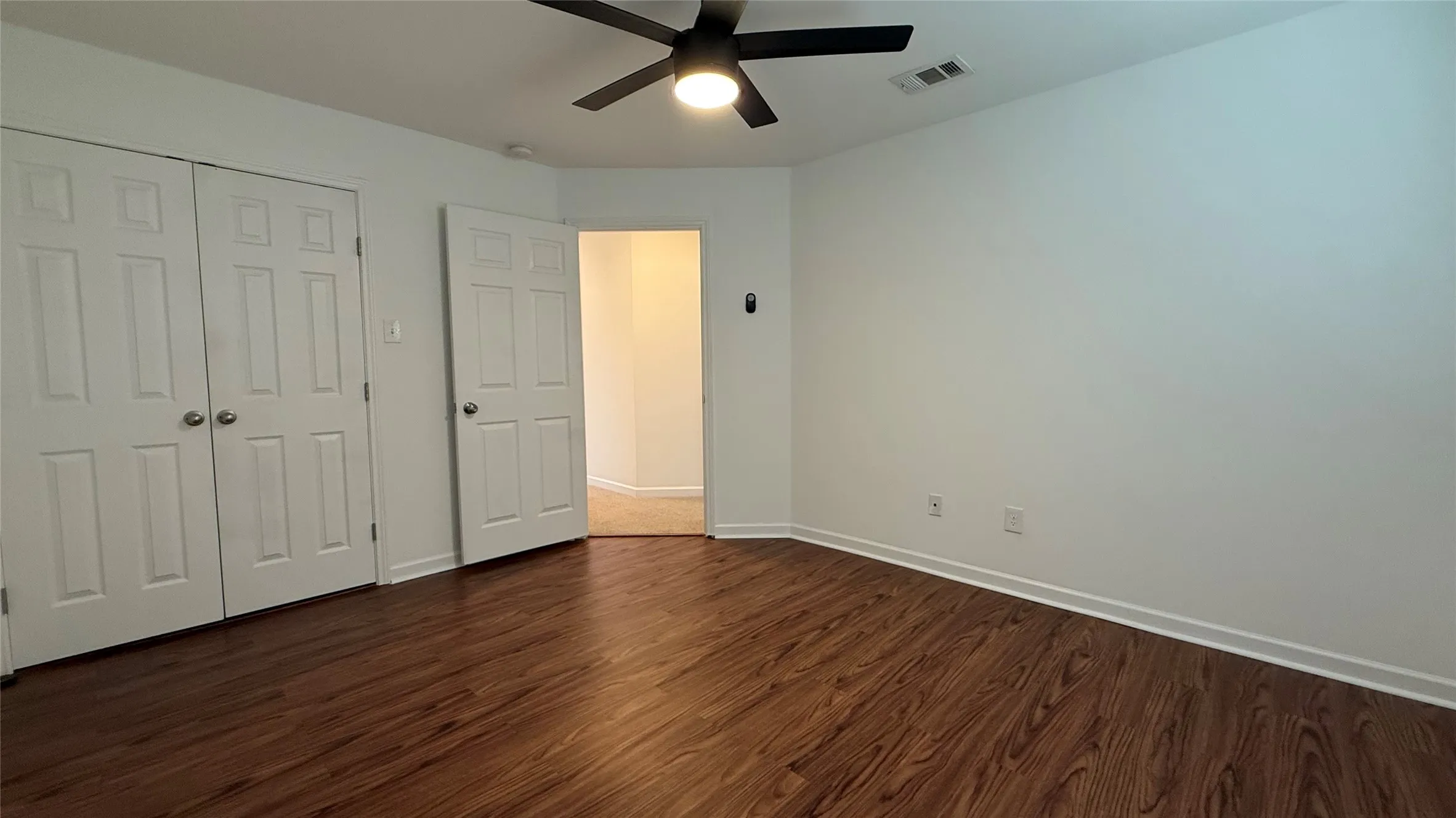 Wood-finish flooring, white paneled doors, ceiling fan with integrated lighting, and white wall finishes