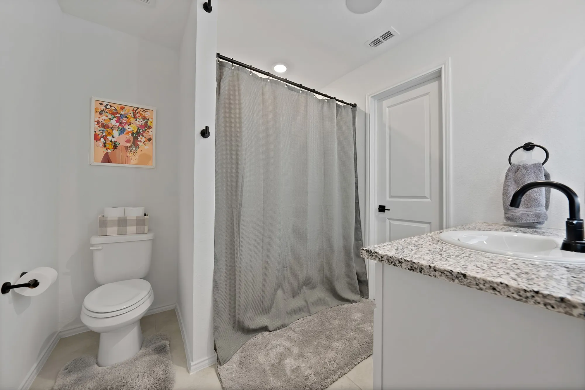 Bathroom featuring a single vanity with stone-finish countertop, integrated sink, matte black faucet, and a shower area with a shower rod