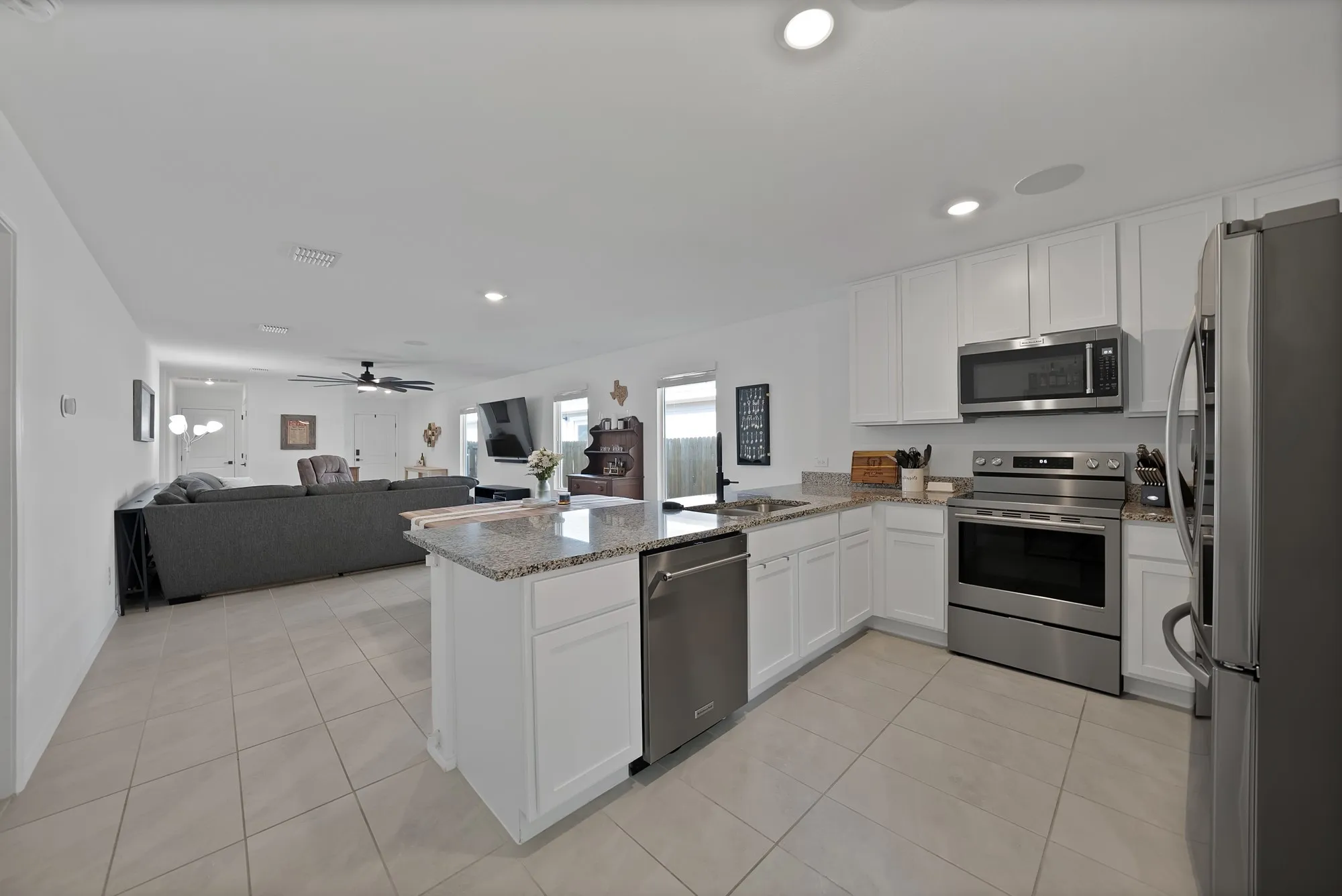 Kitchen featuring white cabinetry, stainless steel appliances, granite countertops, an island with a built-in sink, and tile flooring