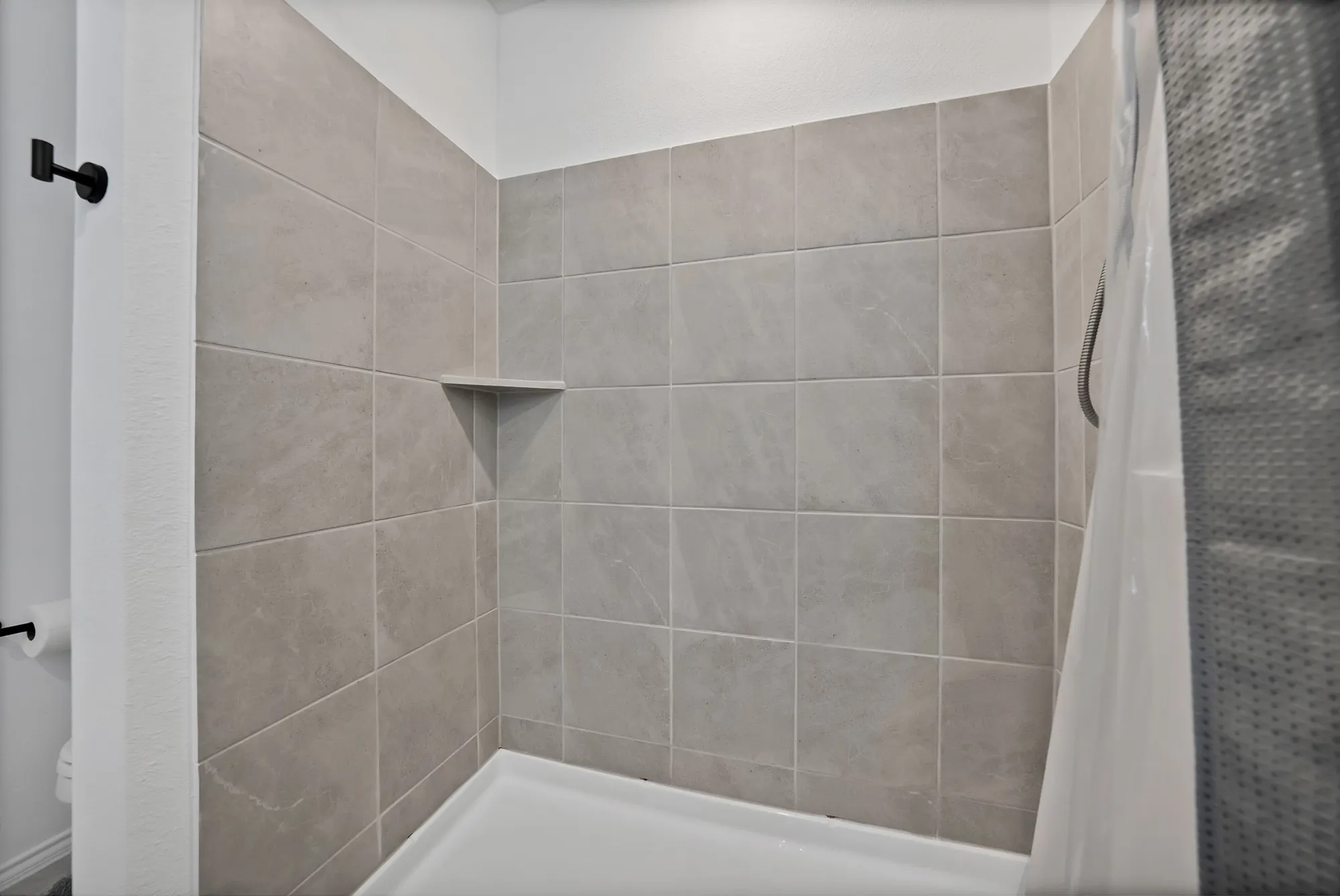 Modern bathroom shower featuring large-format gray ceramic tile walls, a built-in corner shelf, white subway tile accents, and a curved glass shower enclosure with coordinating hardware