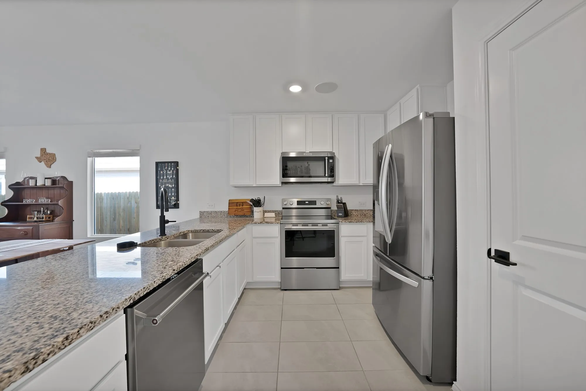 Kitchen featuring white cabinetry, stainless steel appliances, speckled stone countertops, a dual basin sink, and tile flooring