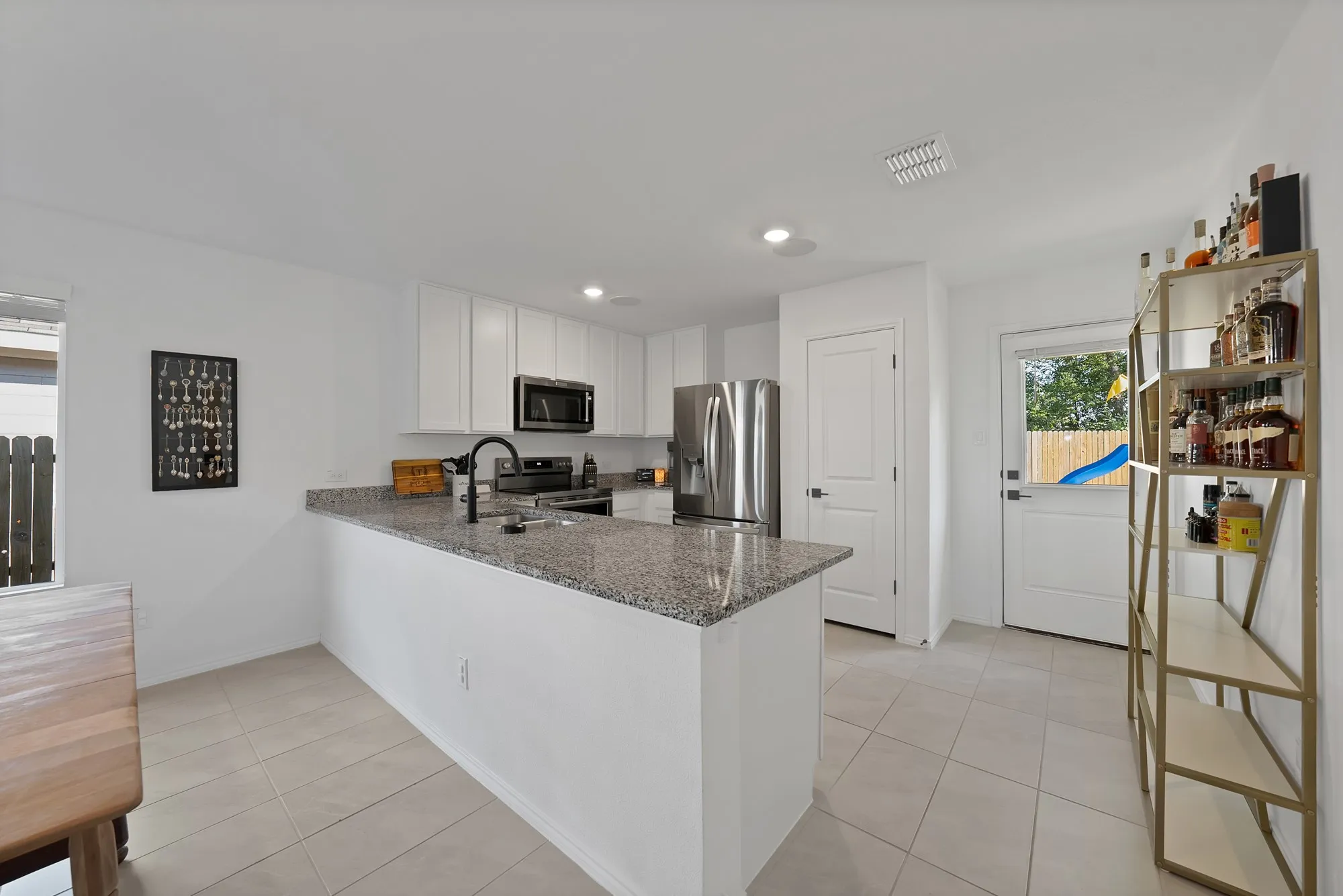 Modern kitchen featuring a large center island with stone countertops, stainless steel appliances including a refrigerator and microwave, white cabinetry, recessed lighting, and tile flooring throughout the open layout