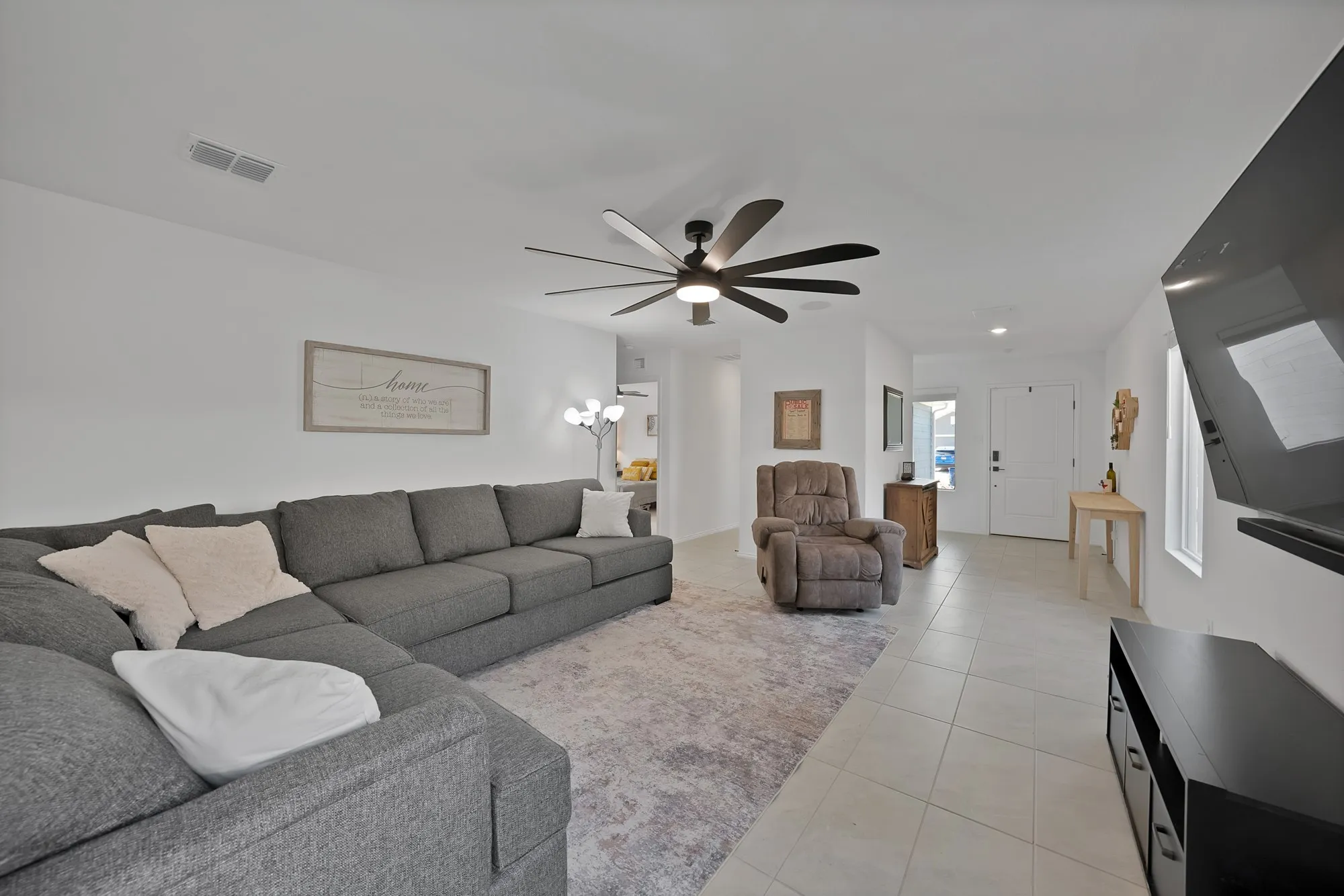 Spacious open-concept living area featuring a sectional layout, tile flooring, and contemporary ceiling fan with integrated lighting