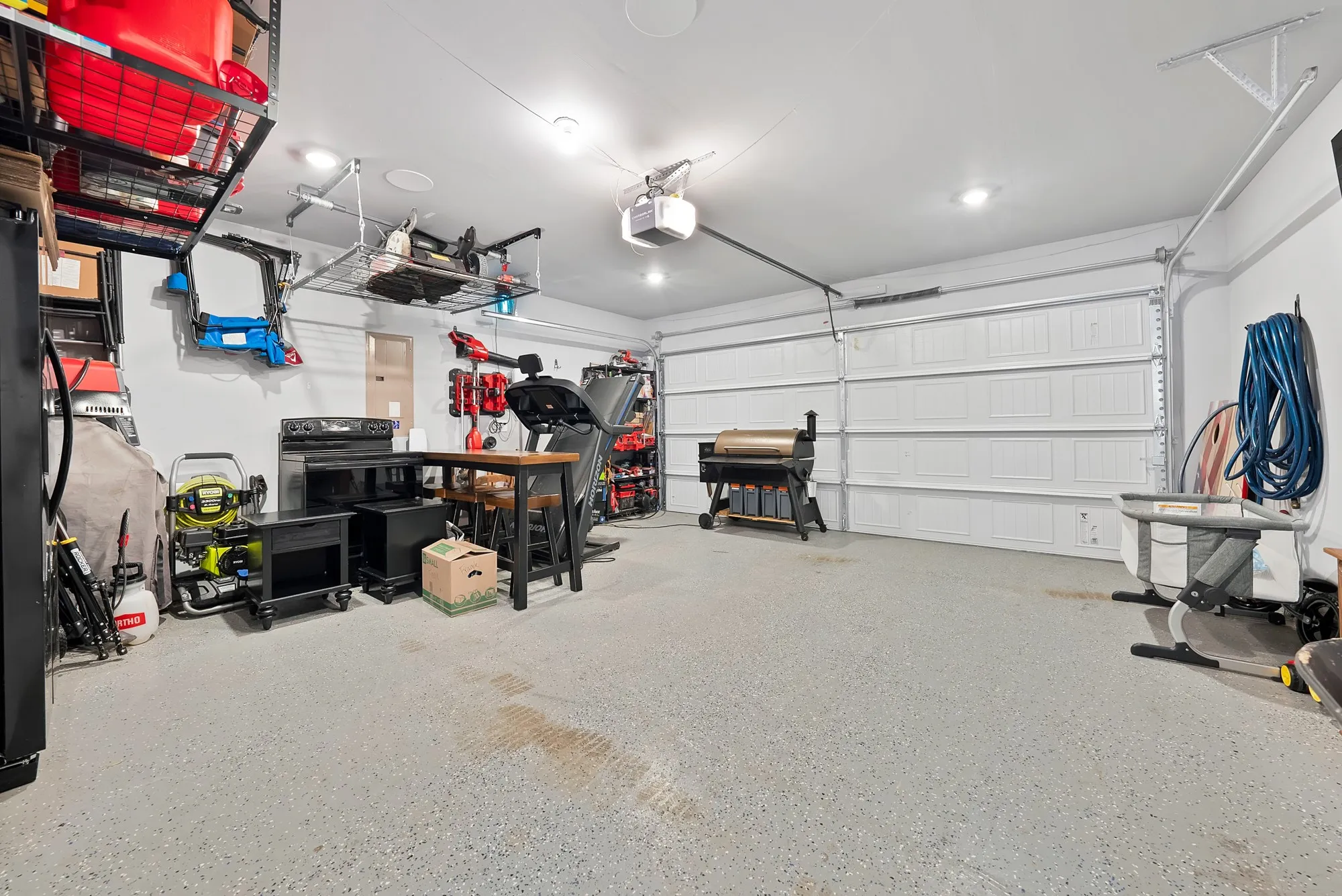 Two-car garage featuring a speckled epoxy floor, recessed lighting, white sectional garage doors, and overhead storage racks
